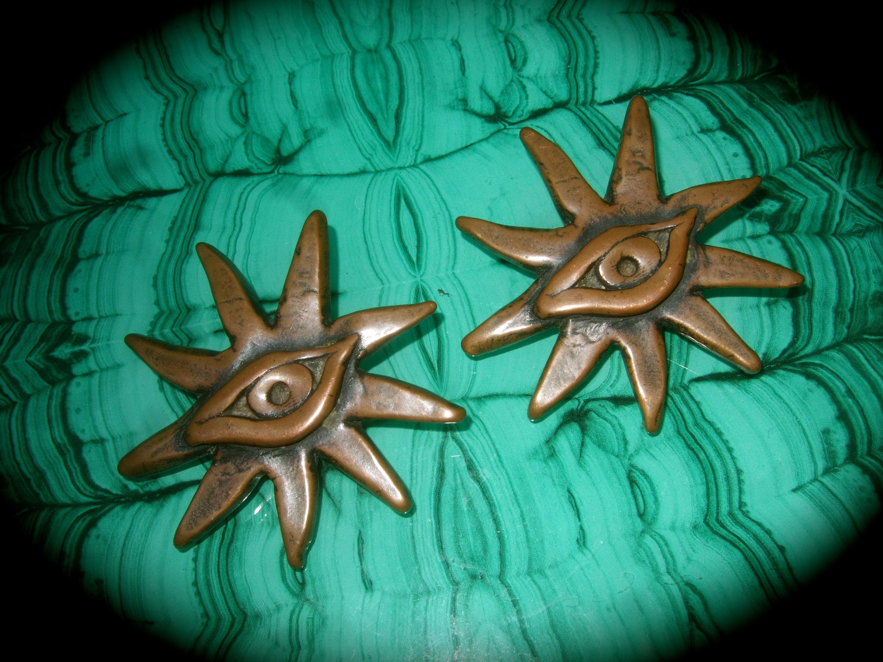French surrealist bronze metal sunburst eye themed clip-on earrings designed by Scooter Paris 
The unique figural large-scale earrings are designed with radiating beams with an eye 
placed in the center 

They make a very bold, avant-garde accessory