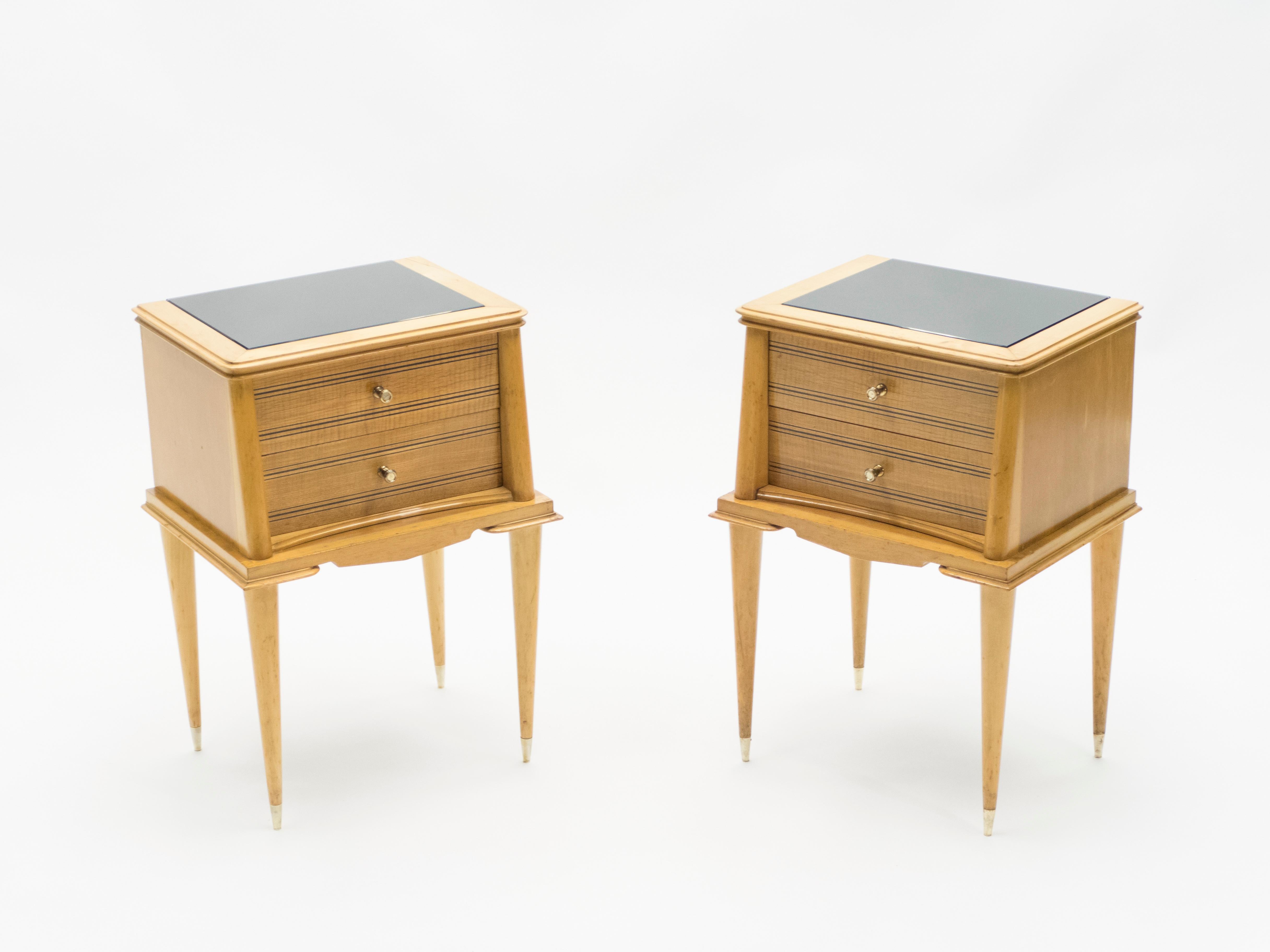 This pair of lined and elegant two drawers nightstands is made from sycamore, with black opaline glass tops, and are attributed to Suzanne Guiguichon, made in the early 1950s. Vintage and sophisticated, they feature brass handles and sinuous saber