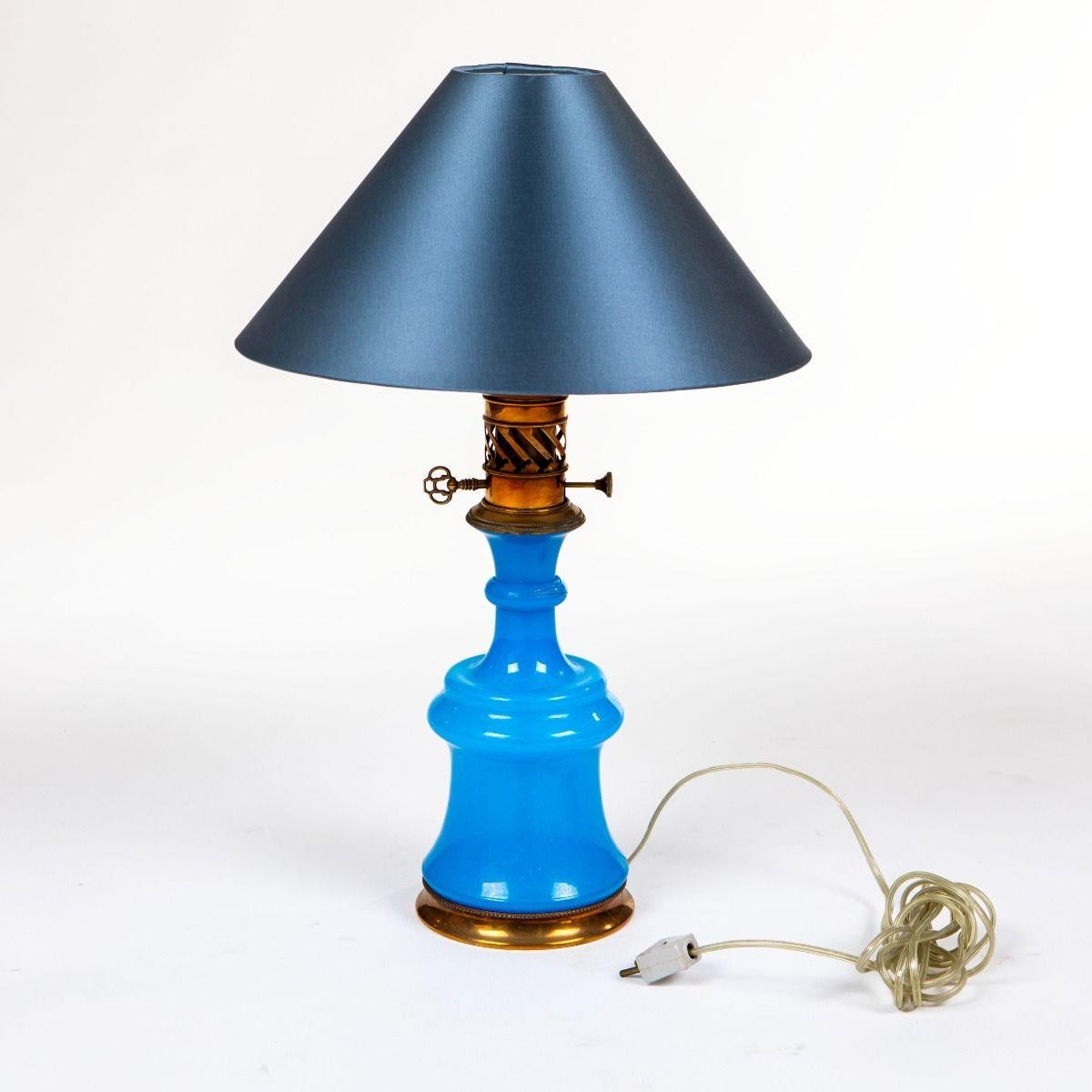Lampe de table française décorative fabriquée en verre opalin bleu vibrant avec d'élégantes montures en laiton.
La lampe est dotée d'une tige en laiton avec des détails à la base et a été conçue à l'origine comme une lampe à huile - aujourd'hui
