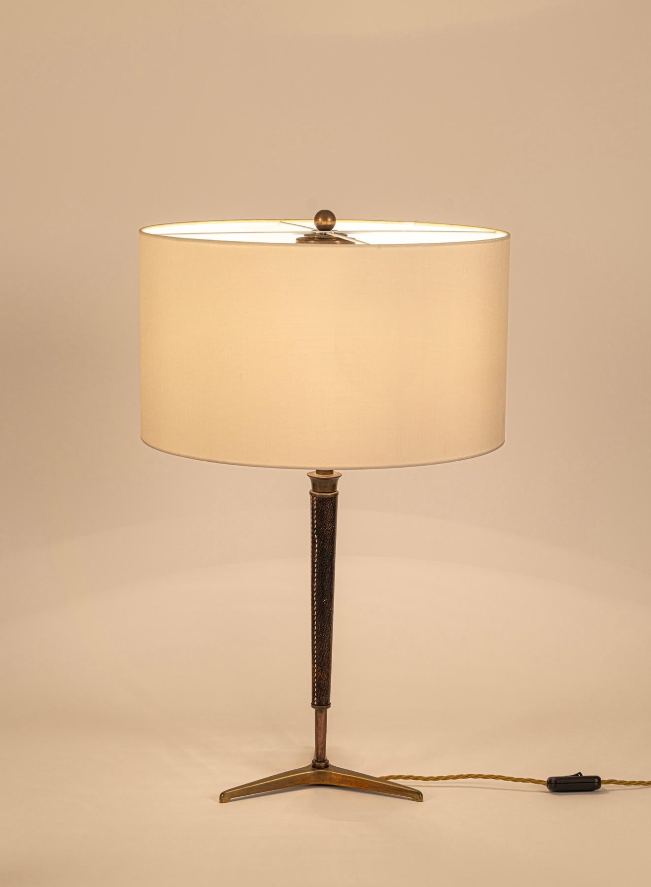 Elegante lámpara de sobremesa con pantalla de seda rehecha.
Vástago de cuero cosido sobre una base de trípode. 
Para 2 bombillas ES