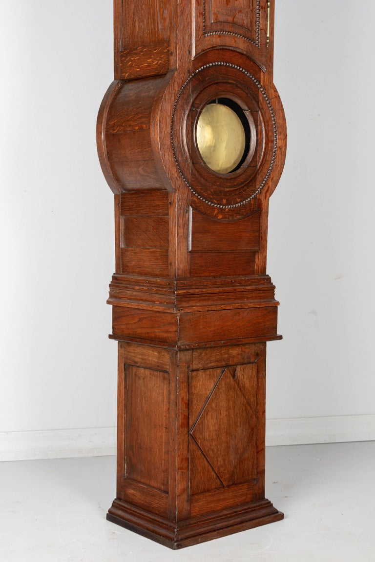 An early 19th century French horloge de parquet, or tall clock, from Normandy. The case is made of solid oak and is in three parts, tapering down at the base and with brass pendulum visible through circular glass window. Unusual construction, with