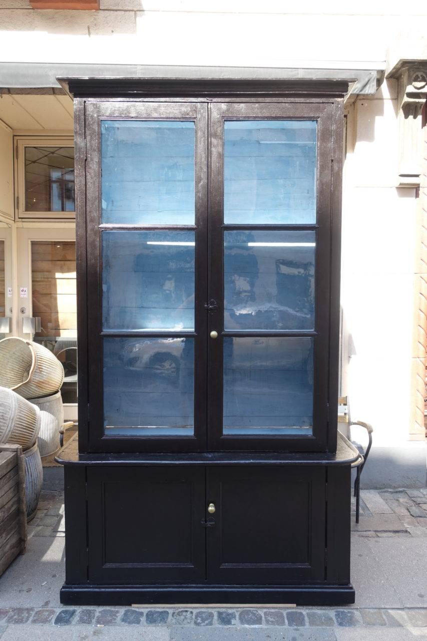 Tall and handsome vintage two part book shelf / display cupboard, from France. Beautiful patina, with its glossy black paintwork, and chalky grey inner. The upper half has two adjustable shelves behind original glass vitrine doors. The lower half