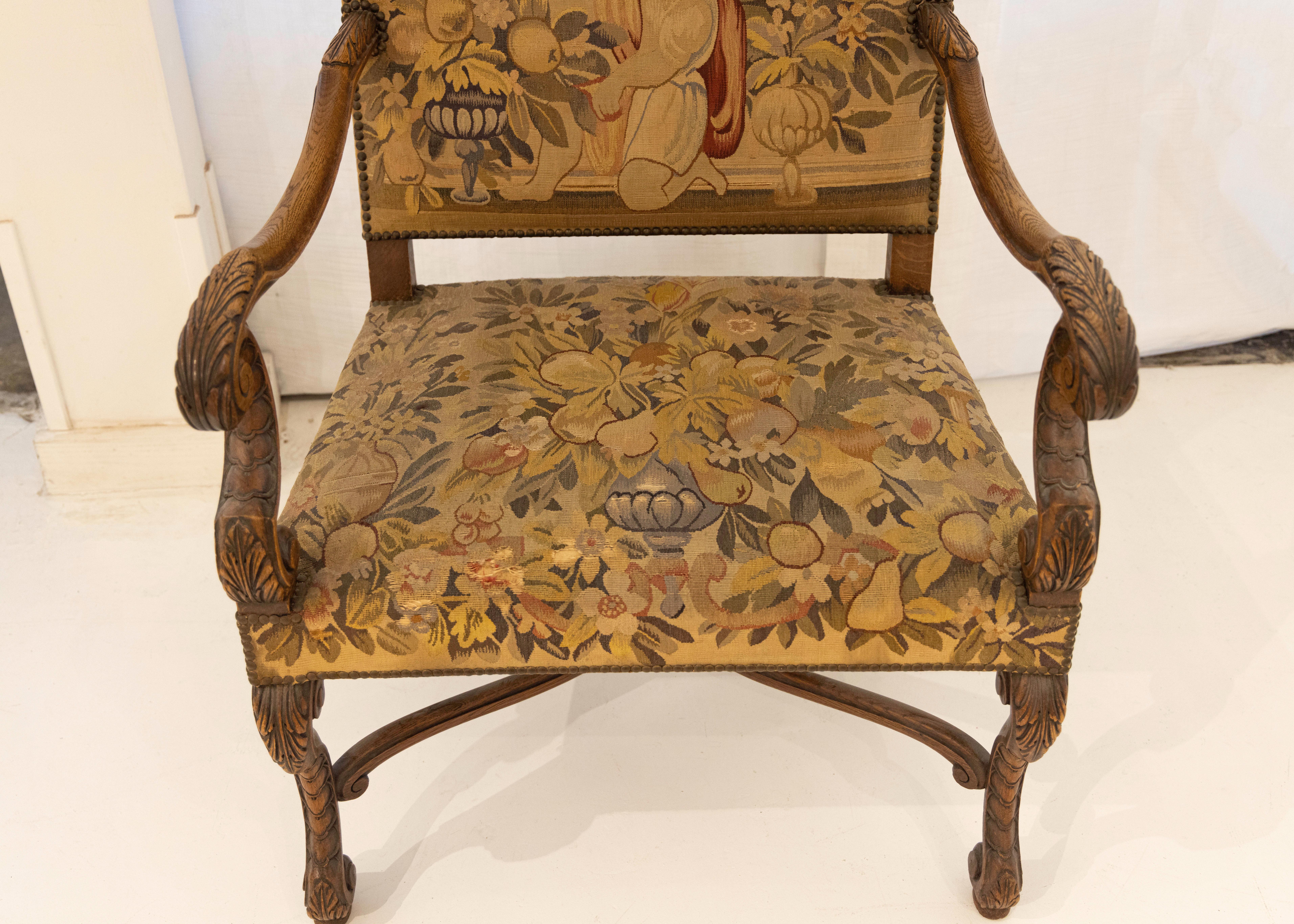 This exquisite French Tapestry chair from the 1700s is a rare gem. It depicts a young boy surrounded by fruit and flowers. The chair has a yellow tint similar to how paintings during this time were painted with yellow ochre undertones. The wood and