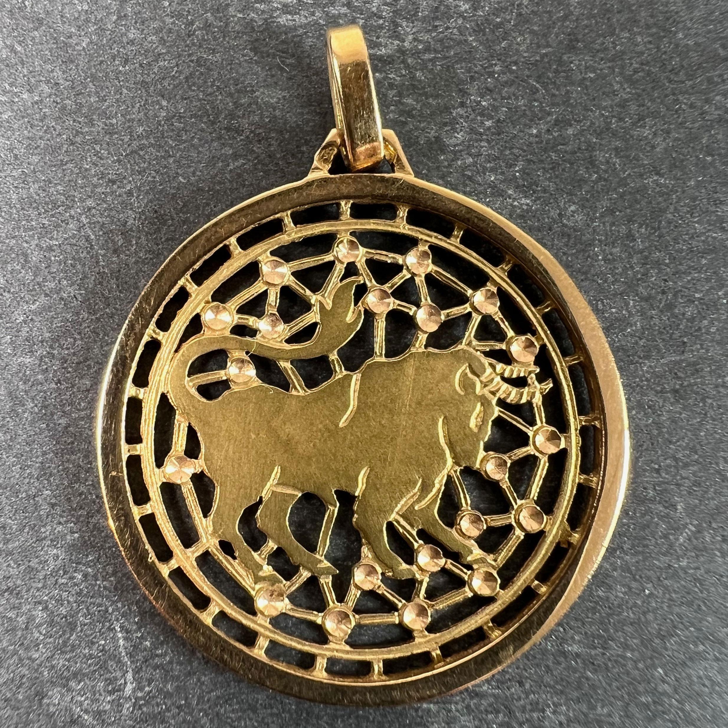 A French 18 karat (18K) yellow gold charm pendant designed as a rouns medal with a pierced background depicting a charging bull representing the zodiac star sign of Taurus on a web of stars. Stamped with the eagle’s head for French manufacture and