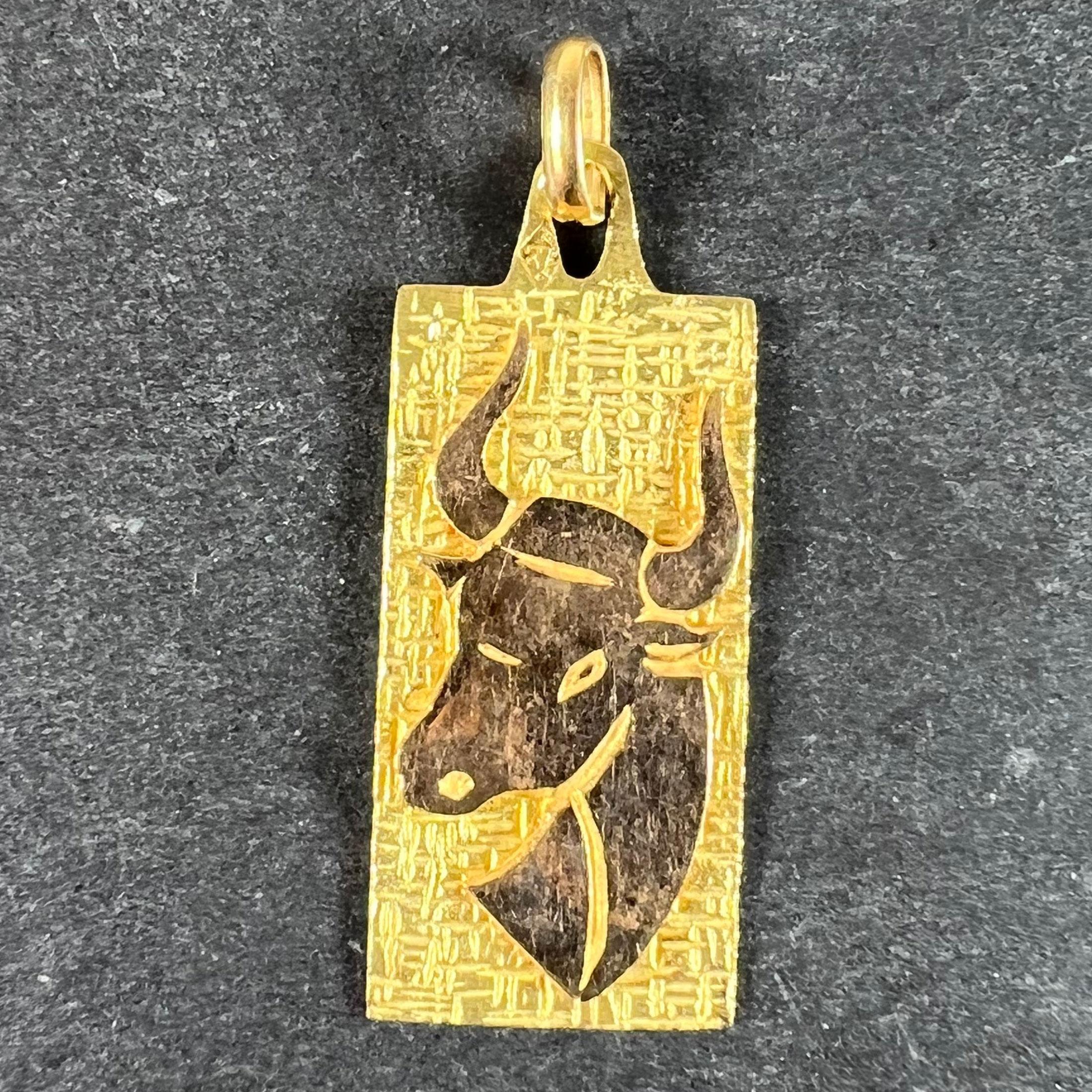 Un ciondolo charme francese in oro giallo 18 carati (18K) disegnato come una medaglia rettangolare che raffigura la testa di un toro con uno sfondo inciso, che rappresenta il segno zodiacale del Taurus. Timbro a testa d'aquila per la manifattura