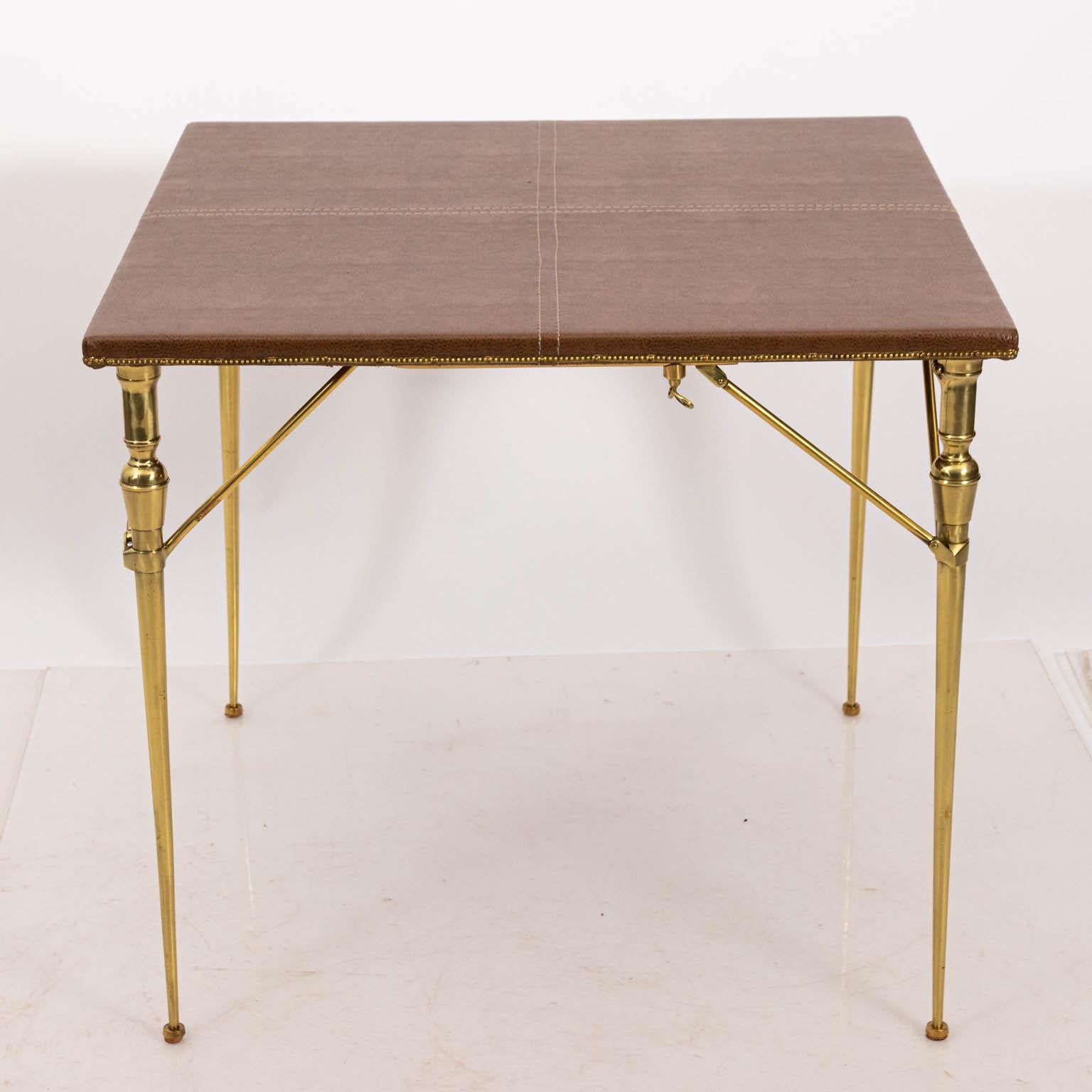 French folding game table in brass and wood with a faux leather top, circa 1930s. The piece also features top stitching with original gold trim throughout. Made in France. Please note of wear consistent with age with newly reupholstered top and