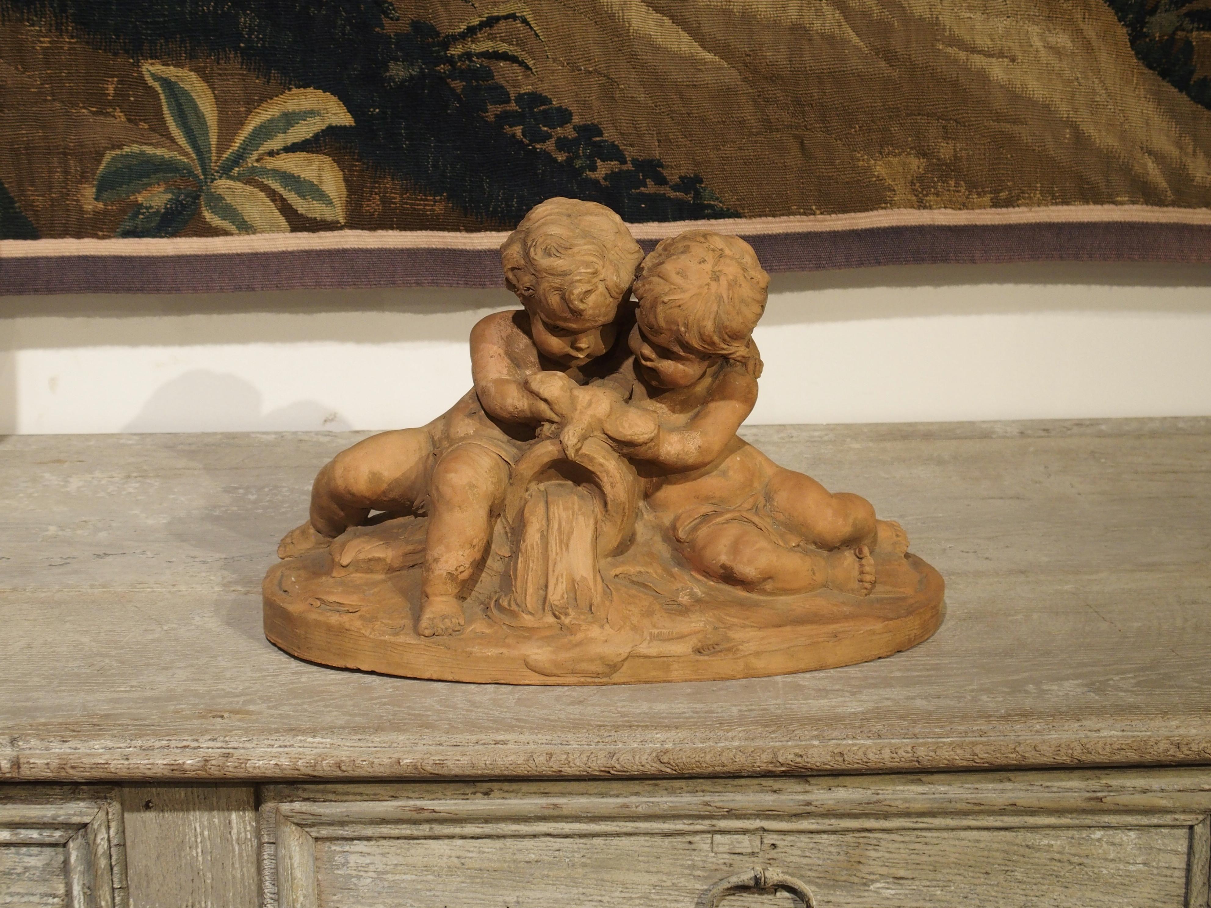 This terracotta was signed by its maker, Fernand Guignier (1902-1972) in the early to mid-20th century. The subject is a tender interpretation of two putti trying to offer a bird some water. There is a wooden keg of water between the putti, which