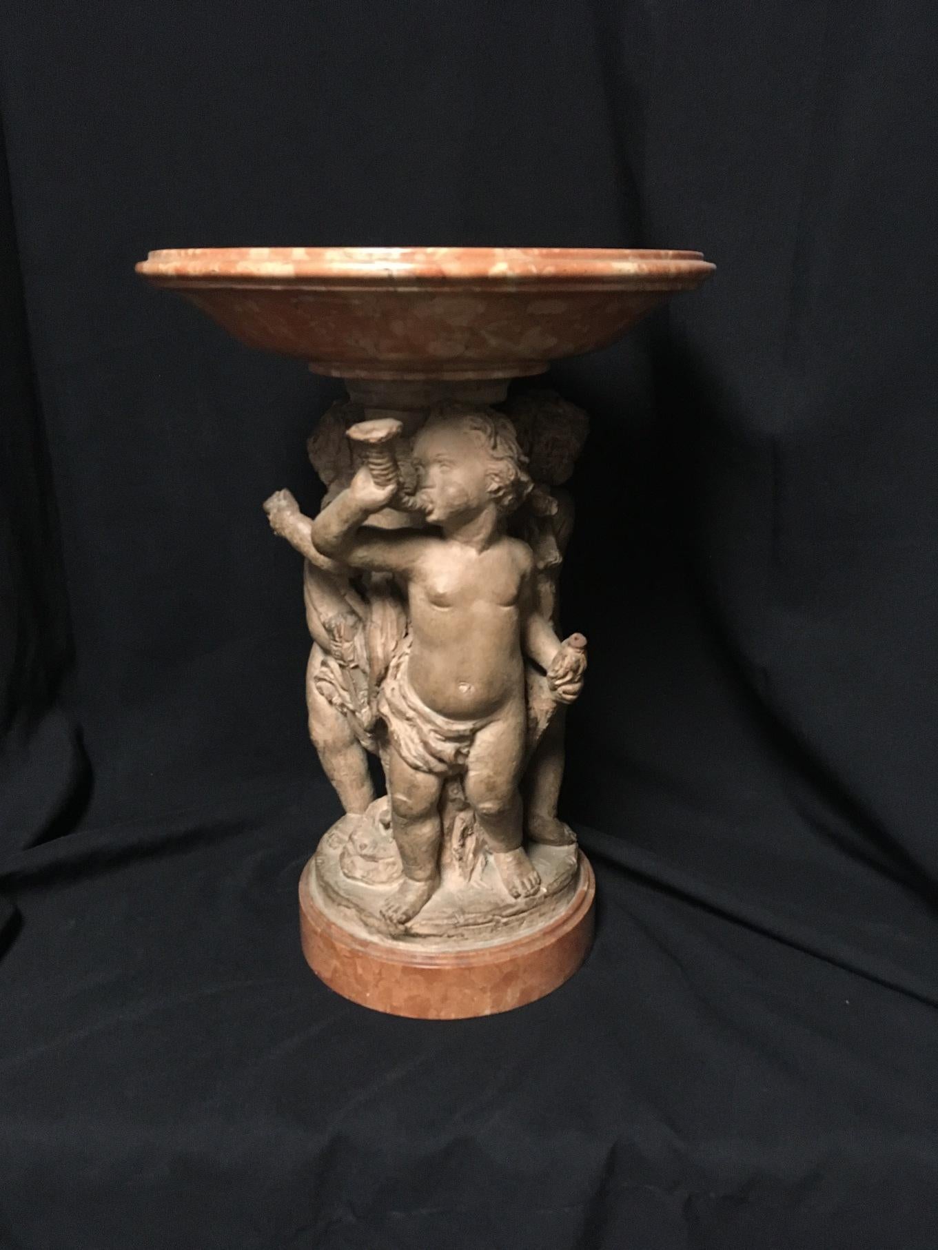 Attractive antique French terracotta and carved marble figural tazza-form centerpiece,
circa 1900.

A hand carved marble bowl rests over a terracotta sculpture depicting three finely sculpted frolicking standing putti, raised on a beautiful round