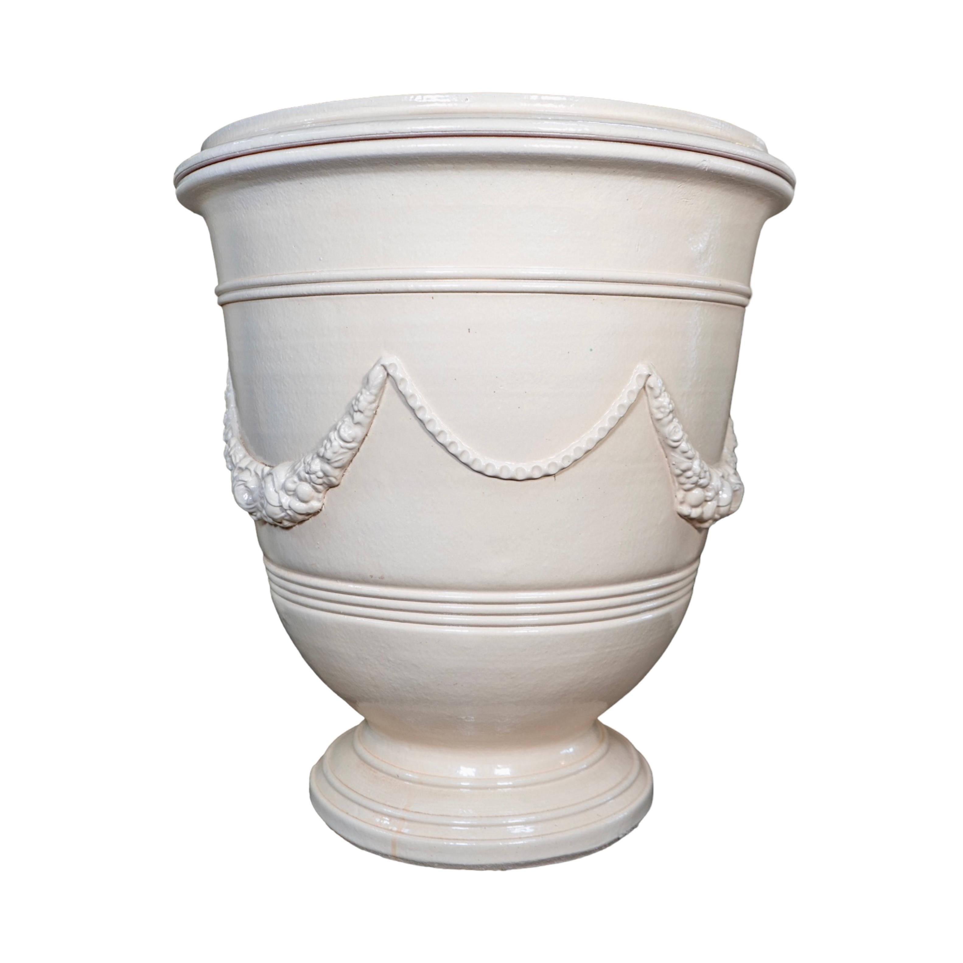 Handmade in France, this French Terracotta Glazed Anduze Planter features an elegant anduze garden wreath swag design with a glazed beige paint finish. Available in two sizes, this is the medium size. It adds a touch of sophistication to any garden