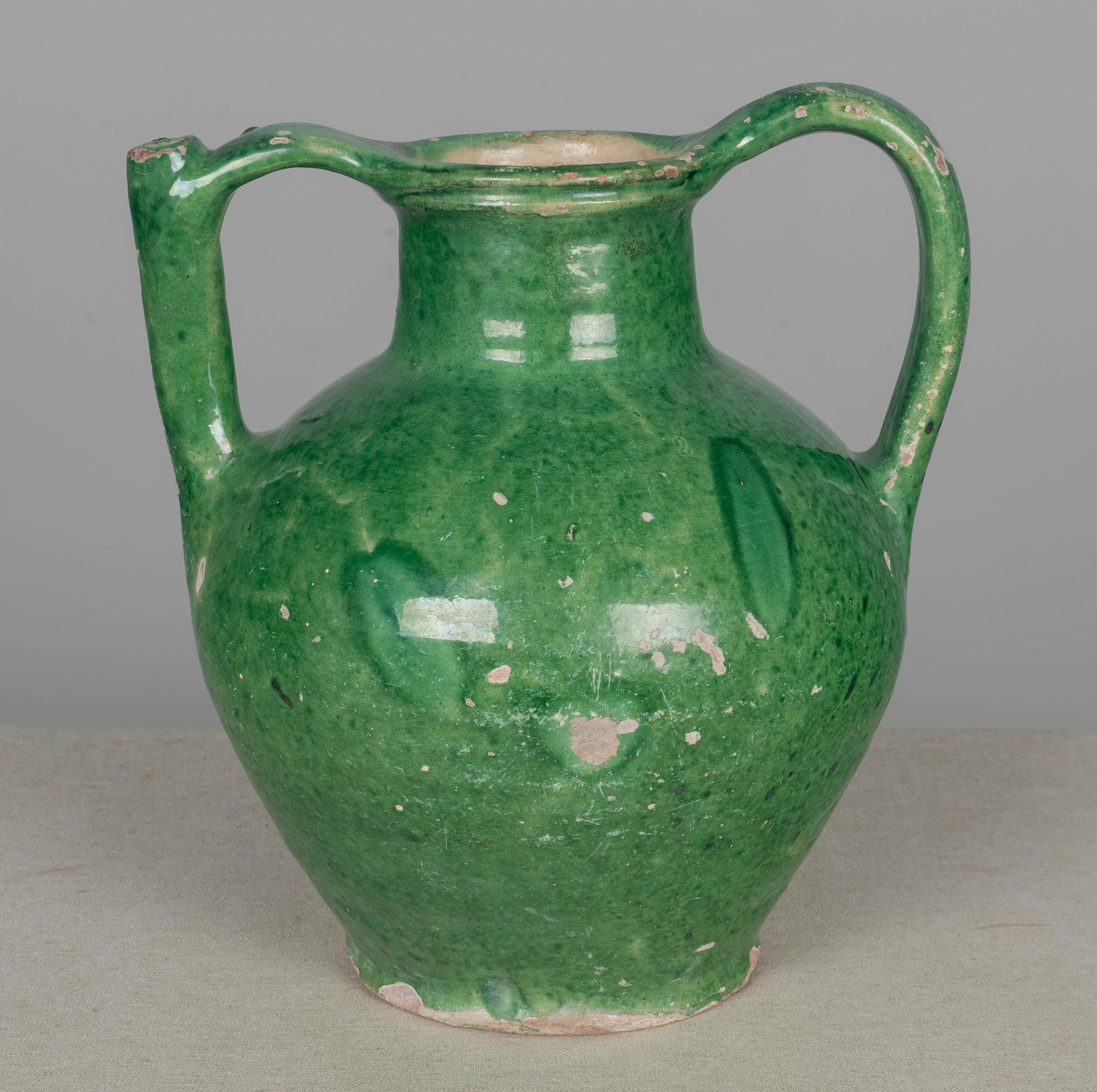 An early 20th century green glazed terracotta vinegar or water jug from the Southwest of France with spout in the handle. Beautiful green color. Chips and losses to glaze. Circa 1900s
Dimensions: 12