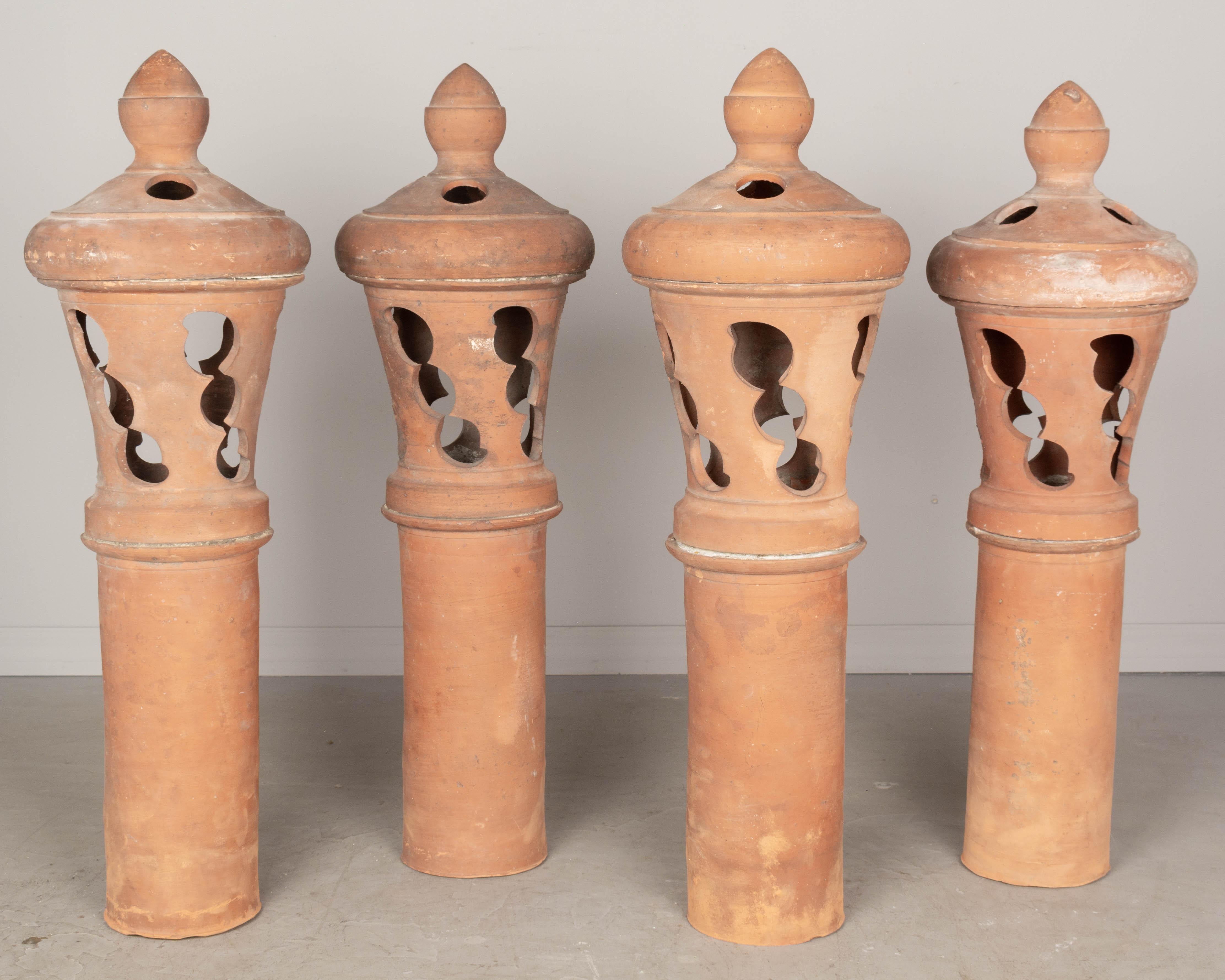 A set of four large French terracotta chimney roof vents. Each in three parts with tall column, decorative cut-out vents and lid with finial. Perfect for use as outdoor garden lanterns. Circa 1900s. 40