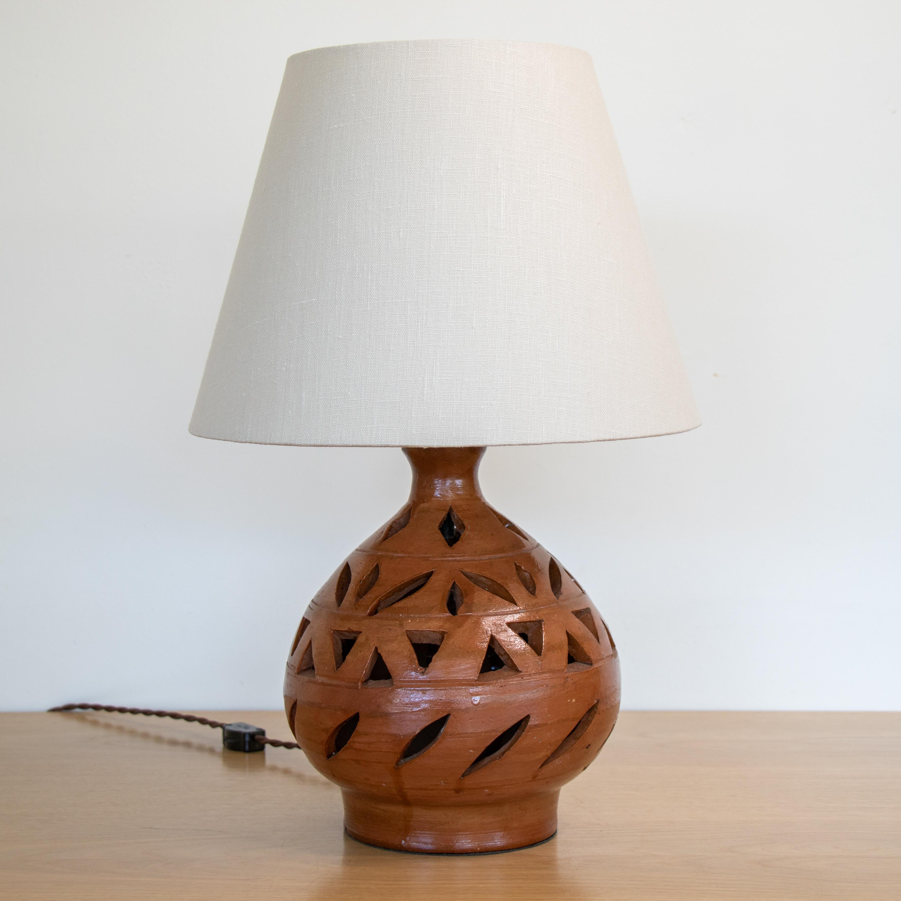 Unique vintage terracotta table lamp from France, 1950's. Jug shape base made of red terracotta with decorative cut outs throughout. Newly rewired and new tapered linen shade. Base measures 9