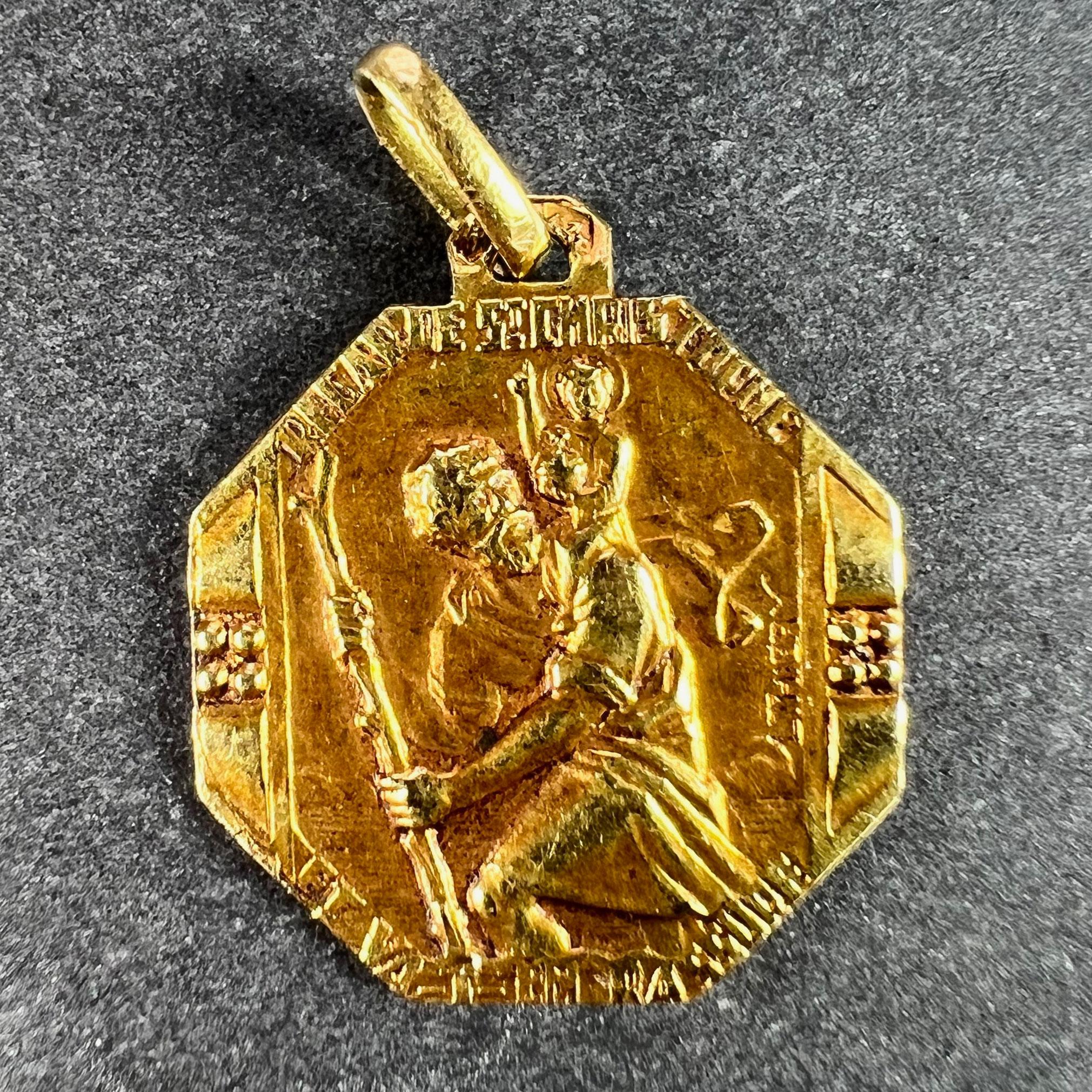 A French 18 karat (18K) yellow gold octagonal charm pendant depicting St Christopher as he carries the infant Christ across a river, with the motto of ‘Regarde St. Christophe et va t’en rassure' around the edge, signed L. Thiery. The reverse depicts