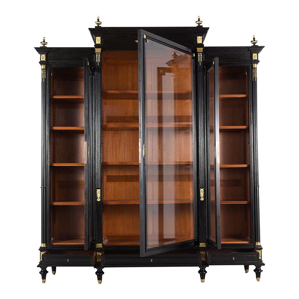 This 19th-century French Louis XVI style bookcase is made out of mahogany wood and has been stained in rich black color with a lacquered finish. This bookcase has two-tiered molded tops, carved columns running down the sides, and it has polished