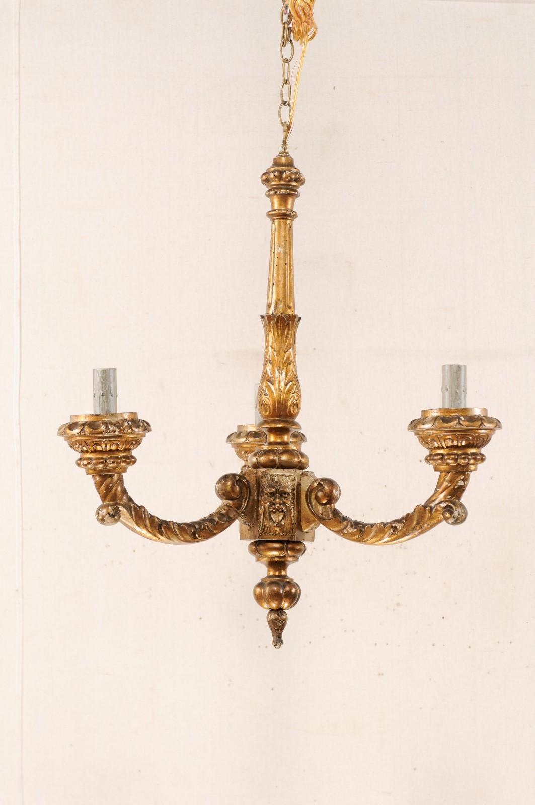 A French three-light gilt and carved wood column chandelier from the mid-20th century. This vintage hanging light from France is adorned with rich acanthus leafs and playful satyr demons motif. Three nicely carved arms extend outward in c-shaped