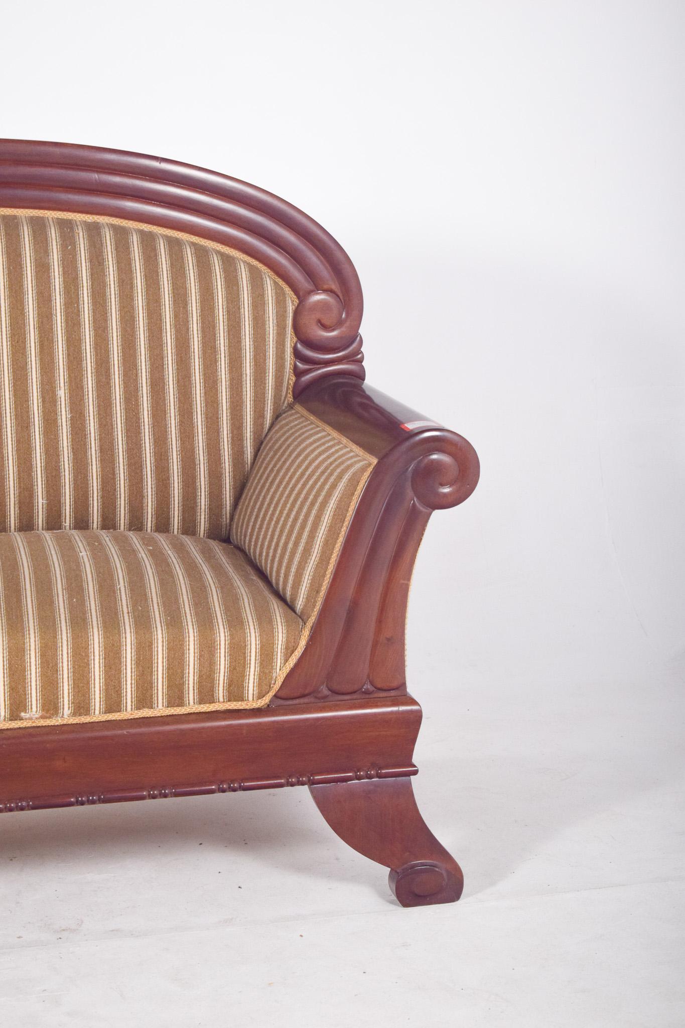 Canapè, rivestito in tessuto a righe. Con uno schienale arrotondato, è circondato da una cornice intagliata con un disegno a volute sui bordi superiori, che conferisce al mobile un'aria di nobiltà e raffinatezza. Anche i braccioli hanno le estremità