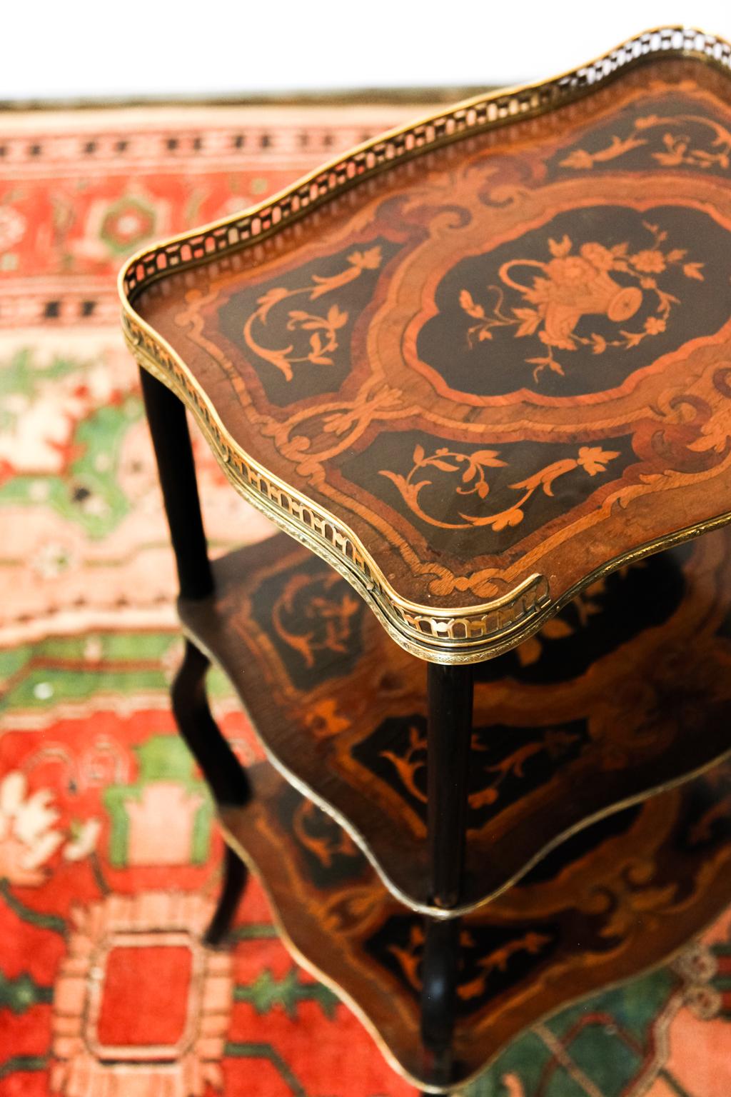 French three-tiered marquetry inlaid table with brass gallery. The shelves are inlaid with baskets of flowers and floral motifs. It is also inlaid with satinwood, birds eye maple, boxwood, and ebony. Each of the three shelves has engraved brass