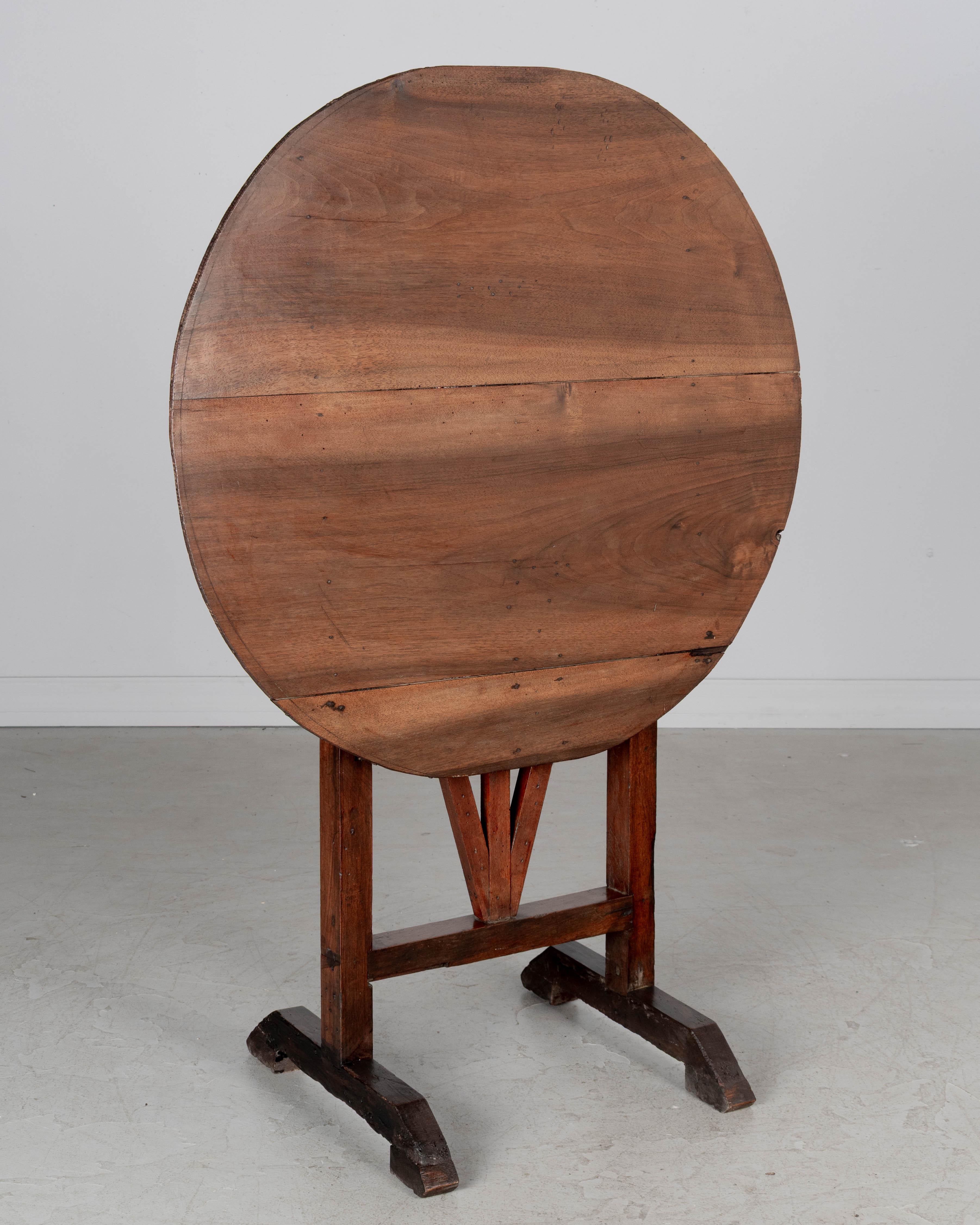 A Country French small tilt-top wine tasting table made of solid walnut. Top has a slightly oval shape made from thin planks of walnut and is sturdy and level. Restoration on legs. Circa 1950-1970.. 
Overall dimensions: 28.75