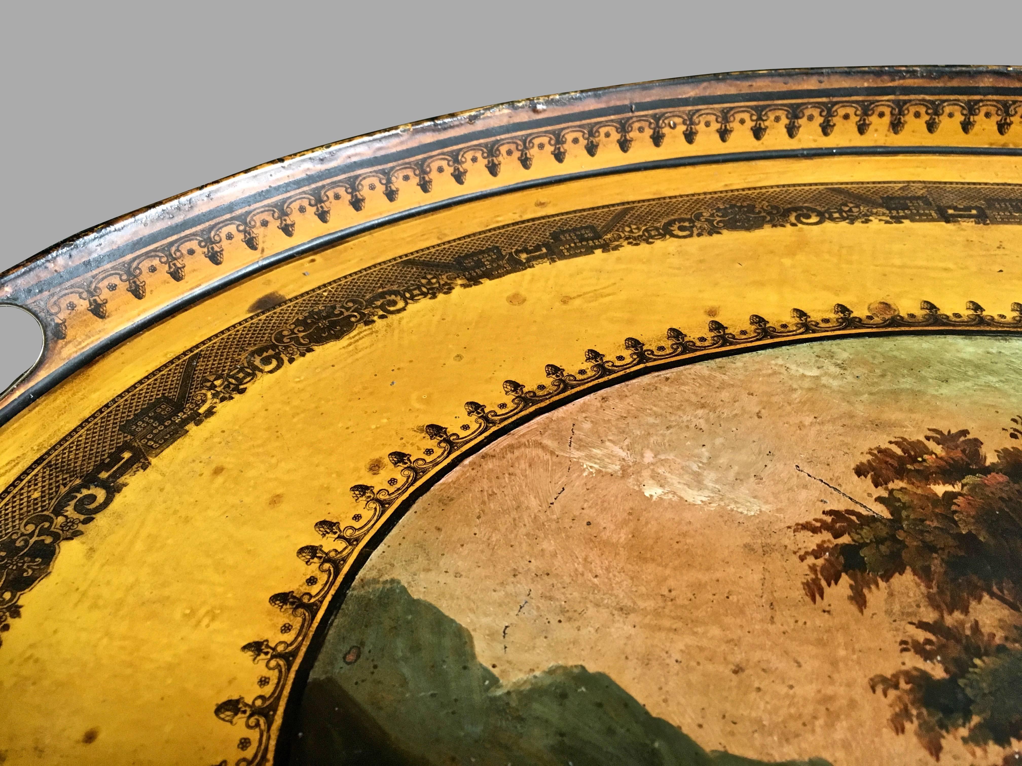 A French yellow ground tole tray decorated with a well-painted central pastoral scene depicting figures in a sunlit valley, the painting surrounded by stenciled decorative black bands, the tray with a flared lip and two cut out handles at each end,