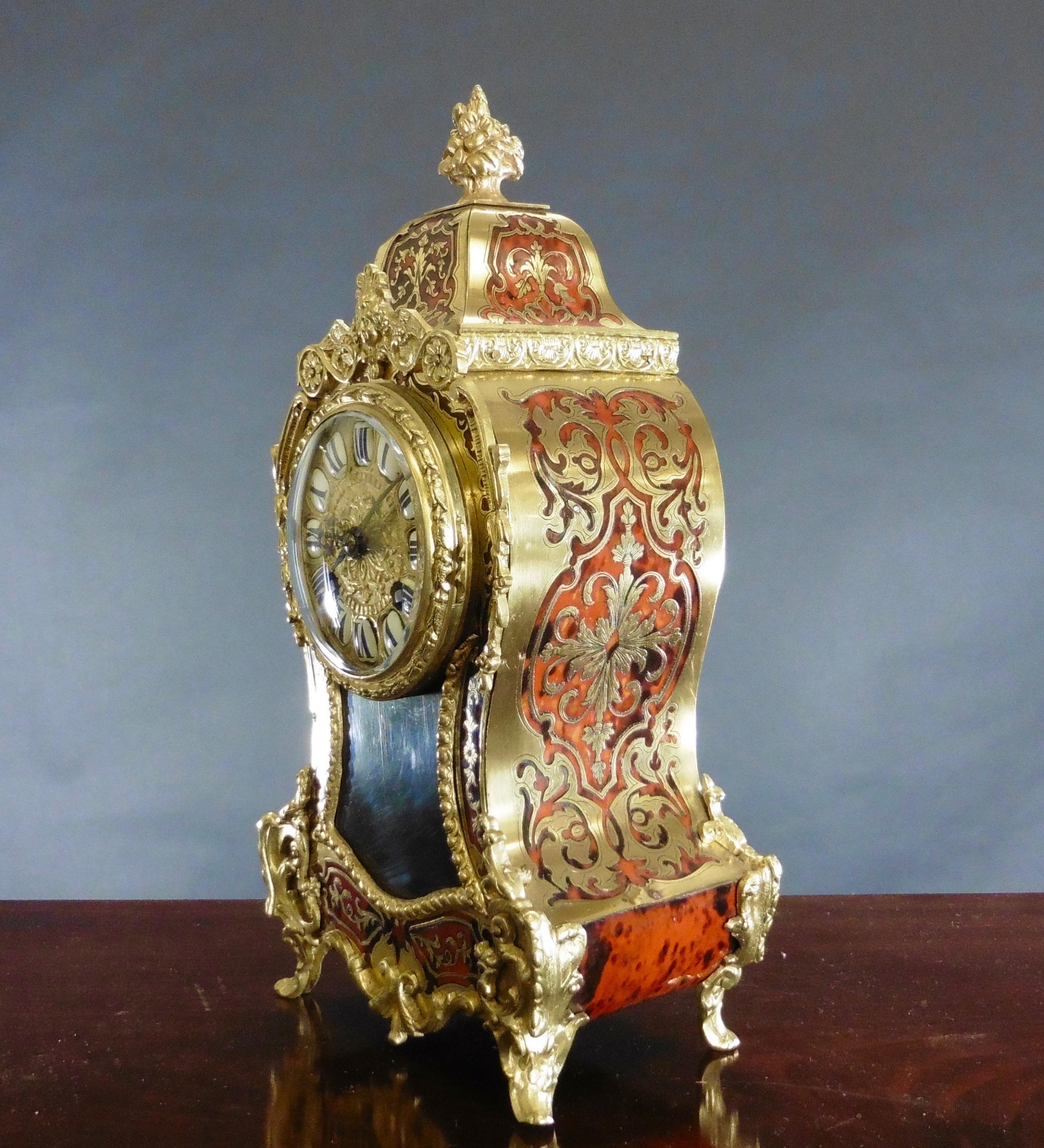 Französische Boulle-Uhr aus Schildpatt mit Ormolu-Beschlägen, die von einem verschnörkelten zentralen Schlussstein gekrönt werden.

Vergoldetes Zifferblatt mit segmentierten römischen Ziffern aus blauem Email.

Acht-Tage-Werk mit Stunden- und