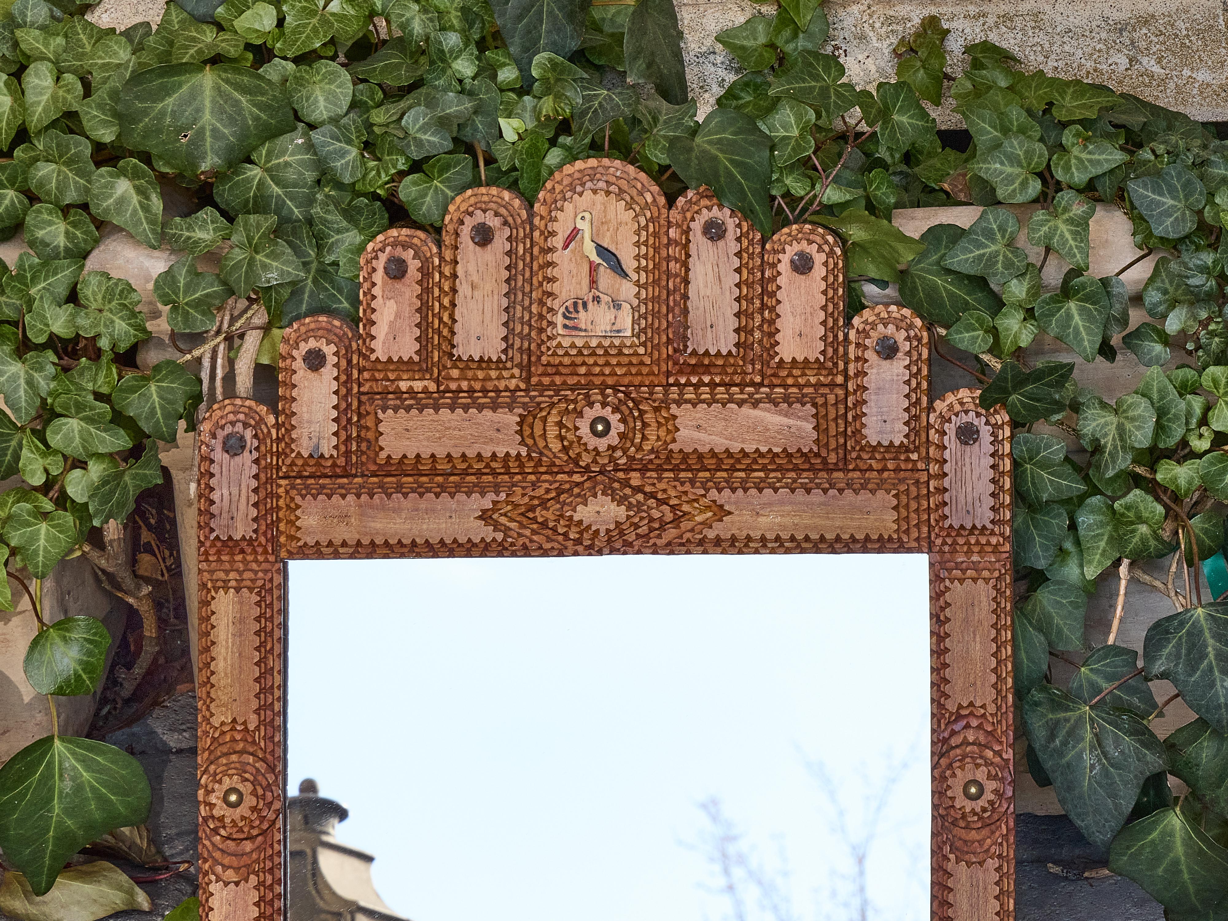 Esempio di artigianato francese della Tramp Art, questo piccolo specchio risale al 1900 circa e si distingue per l'insolita cresta ad arco e per i dettagli dipinti in stile arte popolare. Il telaio è costruito con strati di legno intagliato,