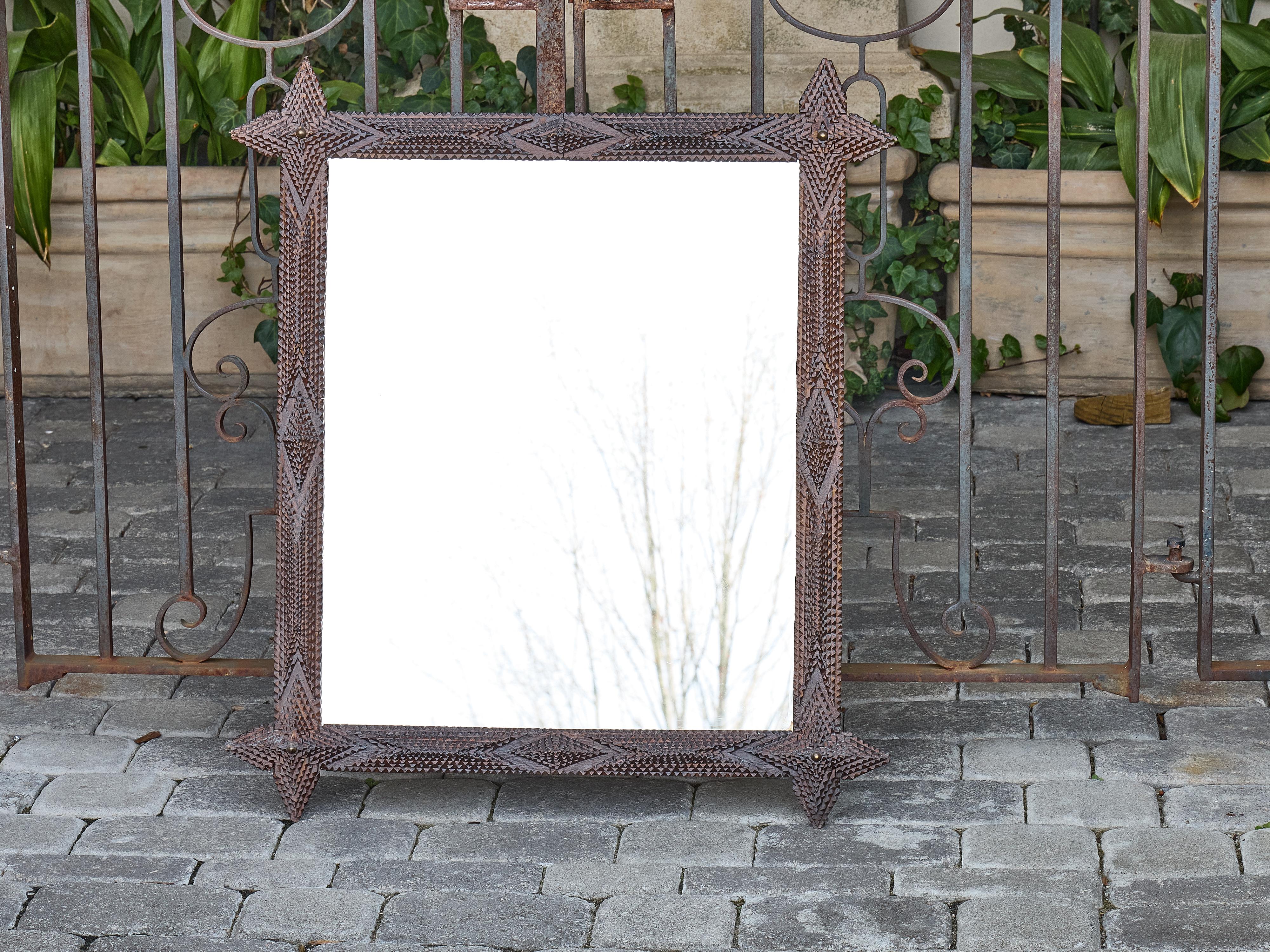 A sculptural French Tramp Art mirror, circa 1900, carved with geometric precision and capped at each corner with sharply notched finials that extend beyond the rectangular frame. The surface is built up in successive layers of chip-carved wood,