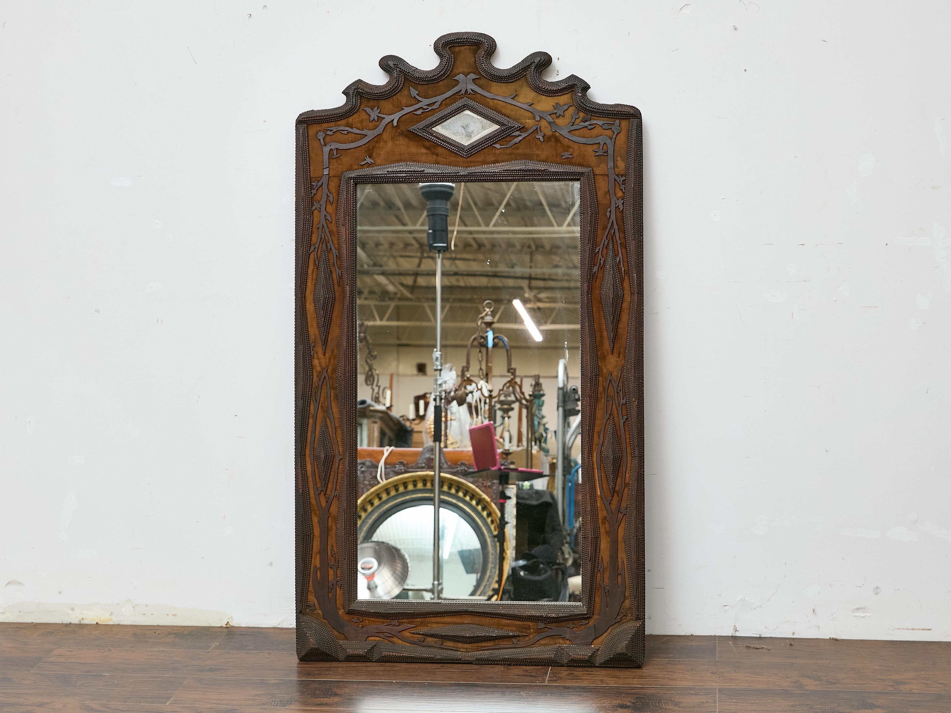 A tall and sculptural French Tramp Art mirror from around 1900, distinguished by its intricate relief carving and decorative texture. The frame is composed of multiple layers of finely chip-carved wood, forming a rhythmic, faceted edge that outlines