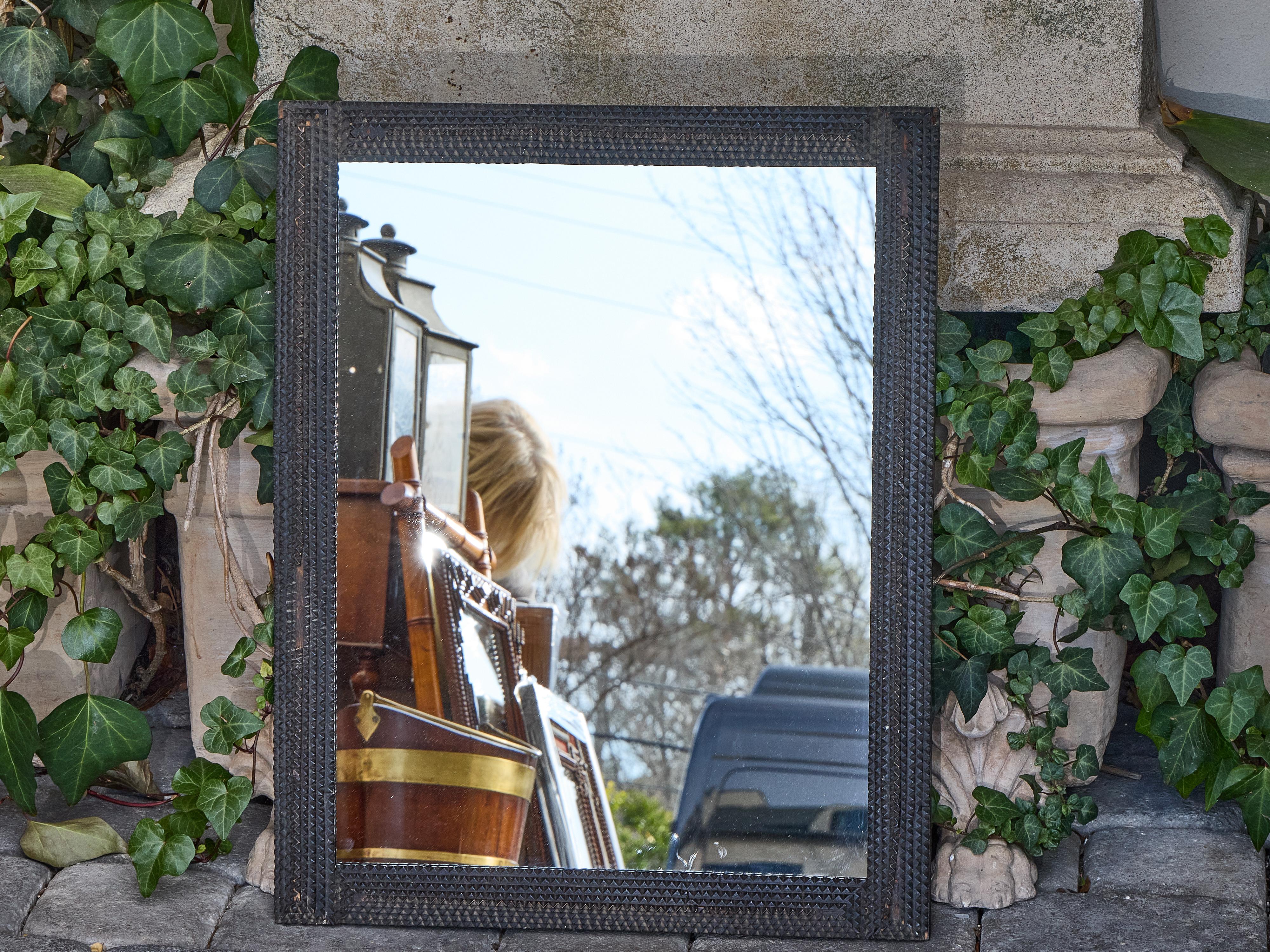 A striking French Tramp Art mirror from the early 20th century, crafted circa 1900 with a distinctive layered chip-carved frame in dark wood. The stepped construction of the surround, built from meticulously notched and stacked elements, creates a