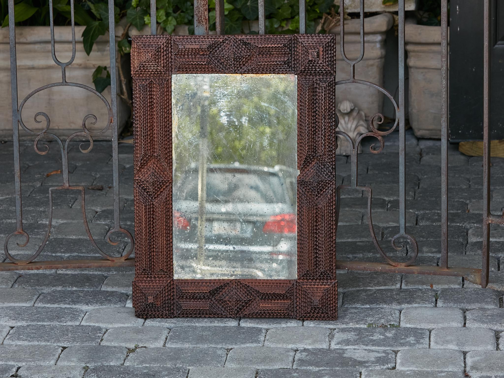 A French Tramp Art hand-carved wooden mirror from the Turn of the Century circa 1900, with raised pyramidal motifs and dark brown patina. Step back in time and embrace the rustic charm of this exquisite French Tramp Art hand-carved wooden mirror