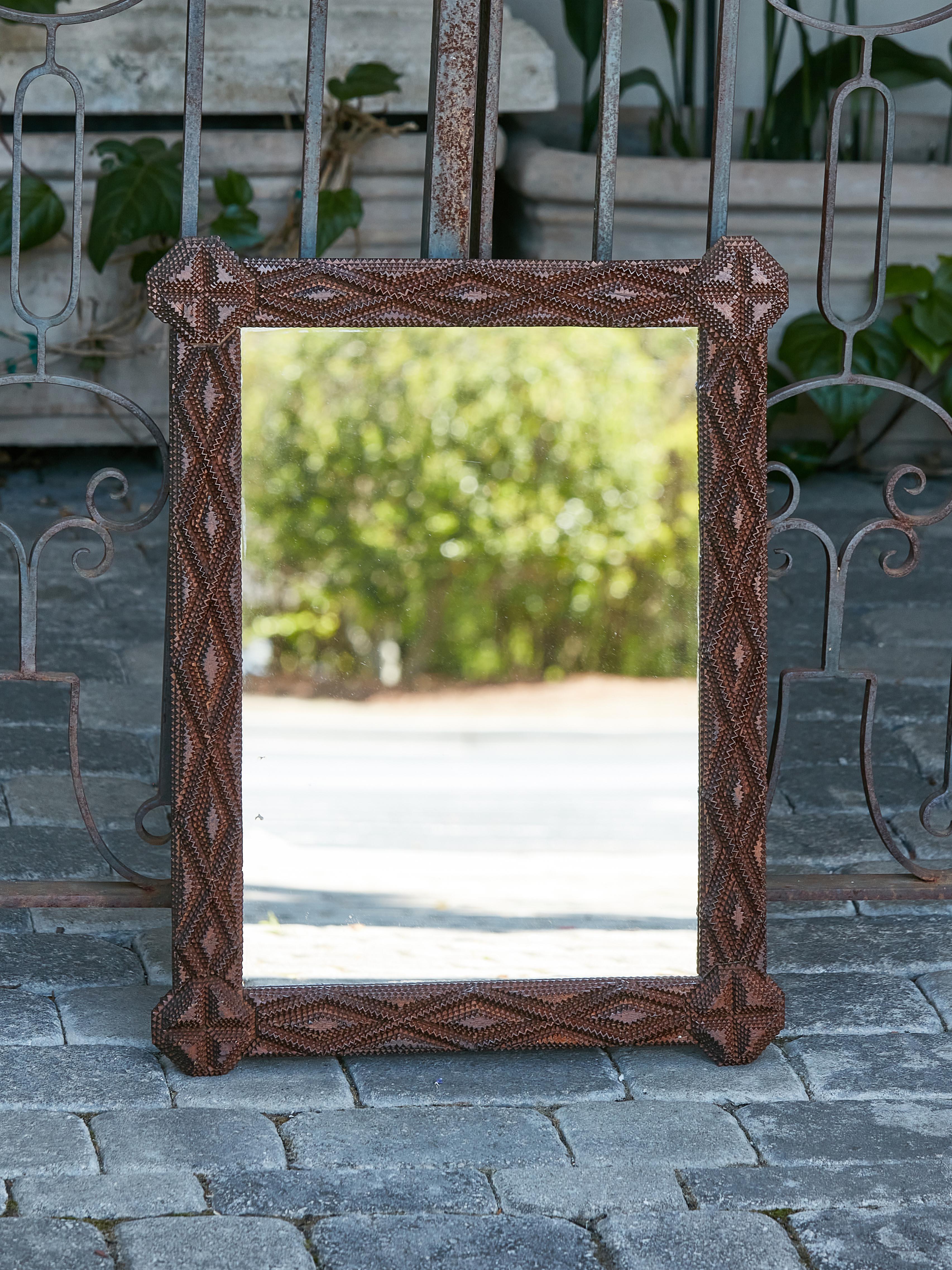 This 1900s French Folk Art Tramp Art period wooden mirror, dating back to the Turn of the Century, features hand-carved geometric motifs, protruding octagonal corners, and a dark brown patina. Immerse yourself in the rich tapestry of French heritage