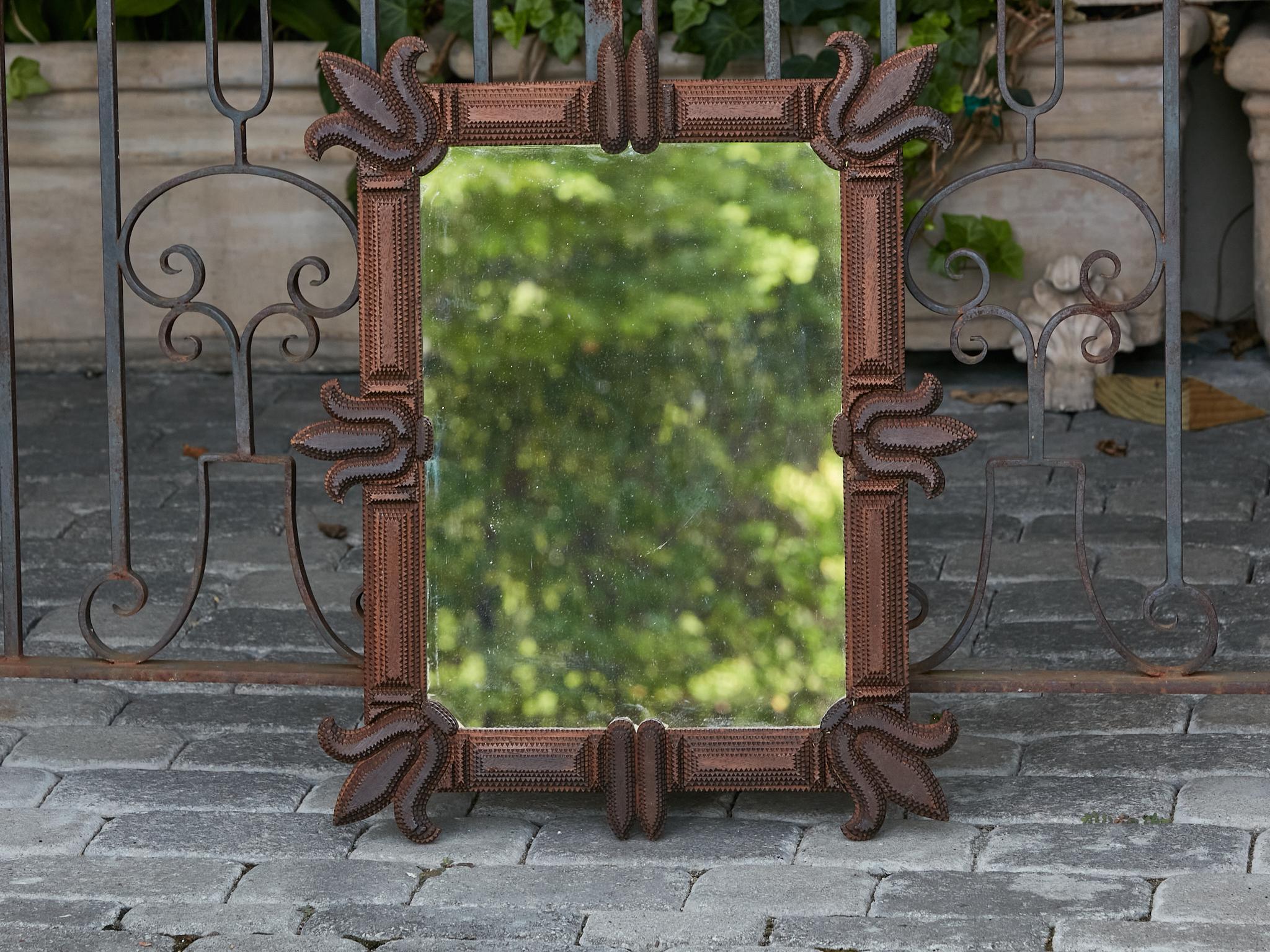A French Tramp Art mirror from the Turn of the Century, with carved flowers in the corners and center of each side. This French Tramp Art mirror, dating from the Turn of the Century, is a captivating blend of folk artistry and understated elegance.