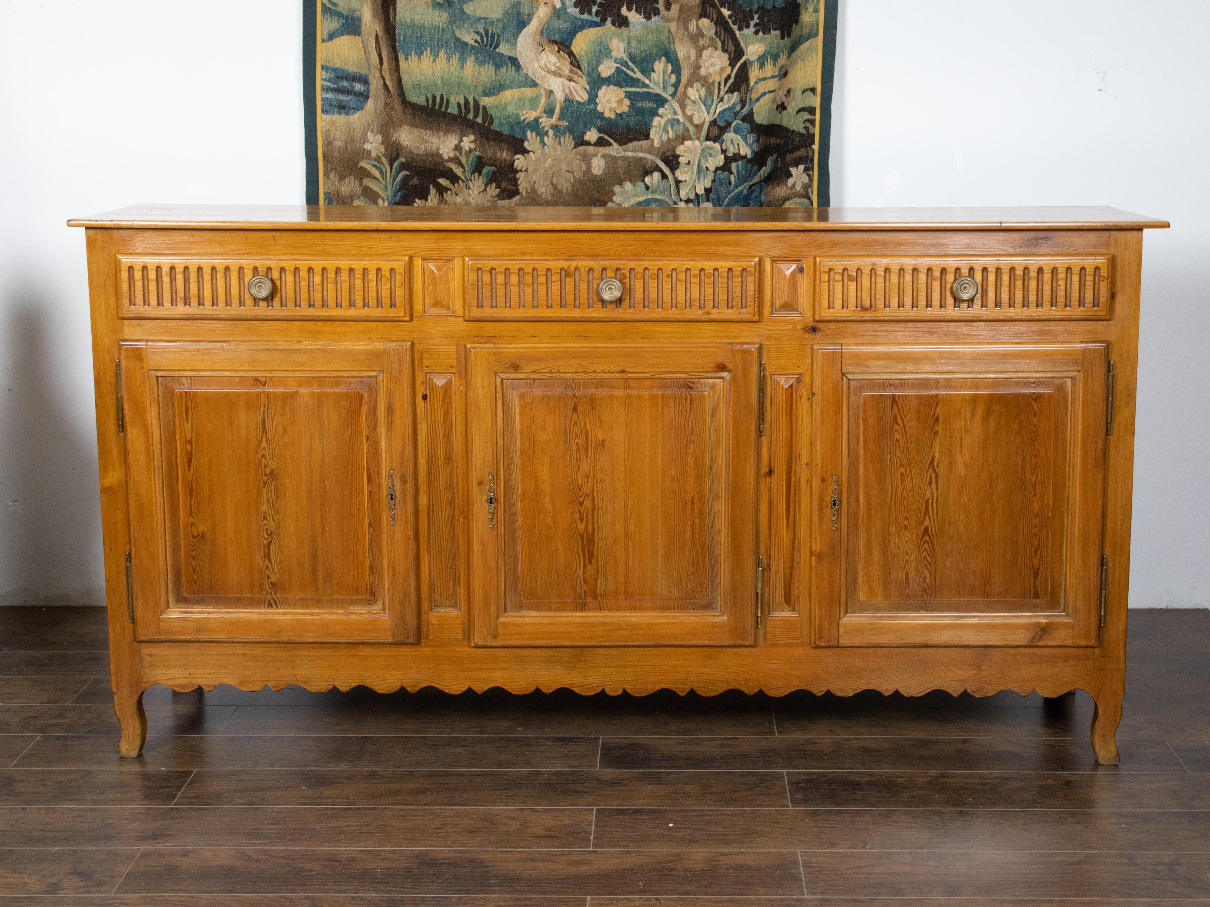 A French Transition style pine buffet from the 19th century, with three fluted drawers over three doors, carved apron and cabriole legs. Created in France during the 19th century, this pine buffet showcases the characteristics of the Transition
