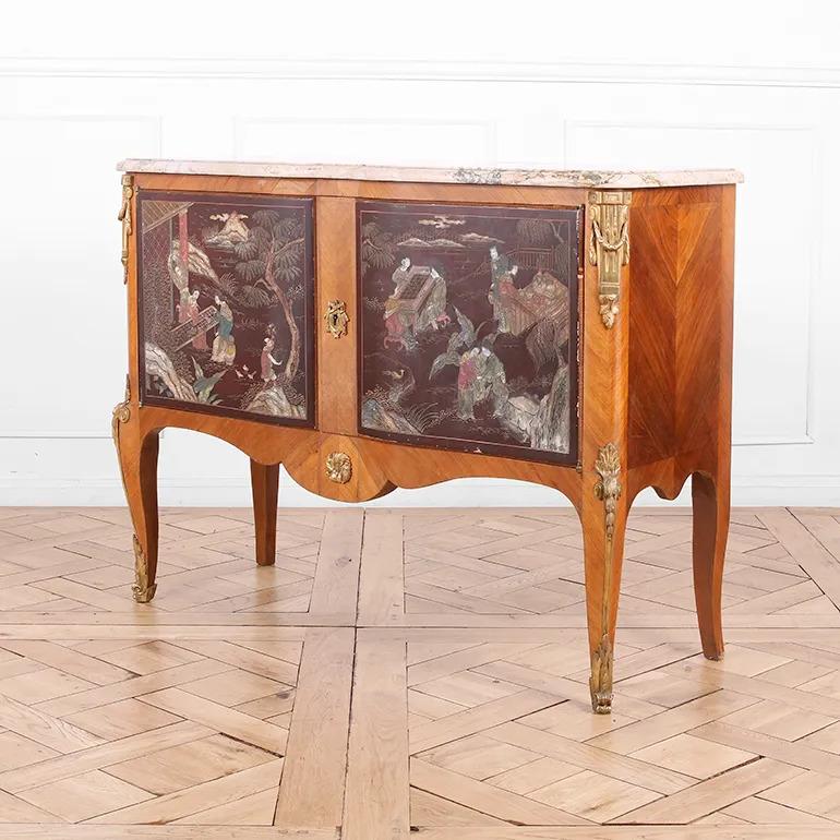 Questa antica commode francese in stile Luigi XV - Transitional è caratterizzata da pannelli laccati a cineserie dipinti a mano che raffigurano scene figurative in un romantico paesaggio orientale, incastonati in una cornice in legno di tulipano e