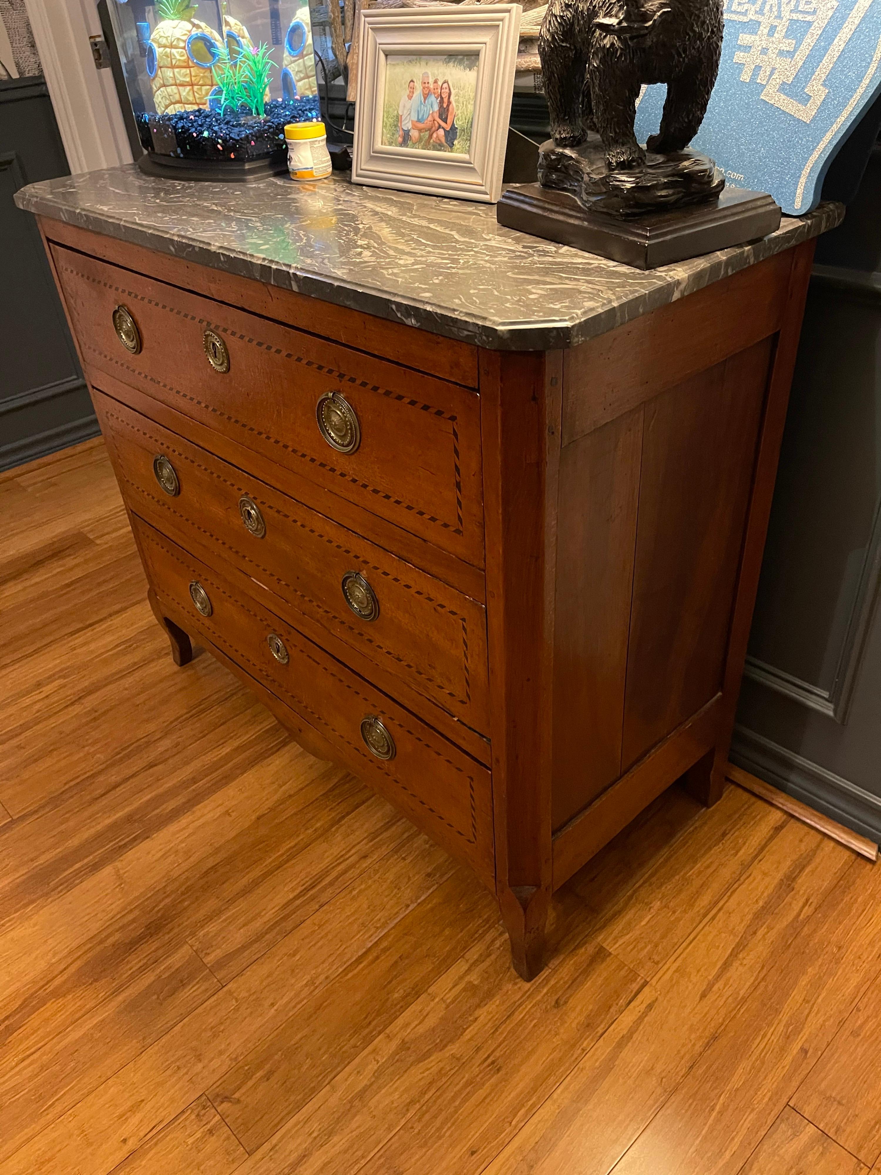 Beautifully patinated French Transitional style mahogany commode with a black marble top above parquetry inlaid accented drawers with original brass pulls and escutcheons. Great traditional look!!
