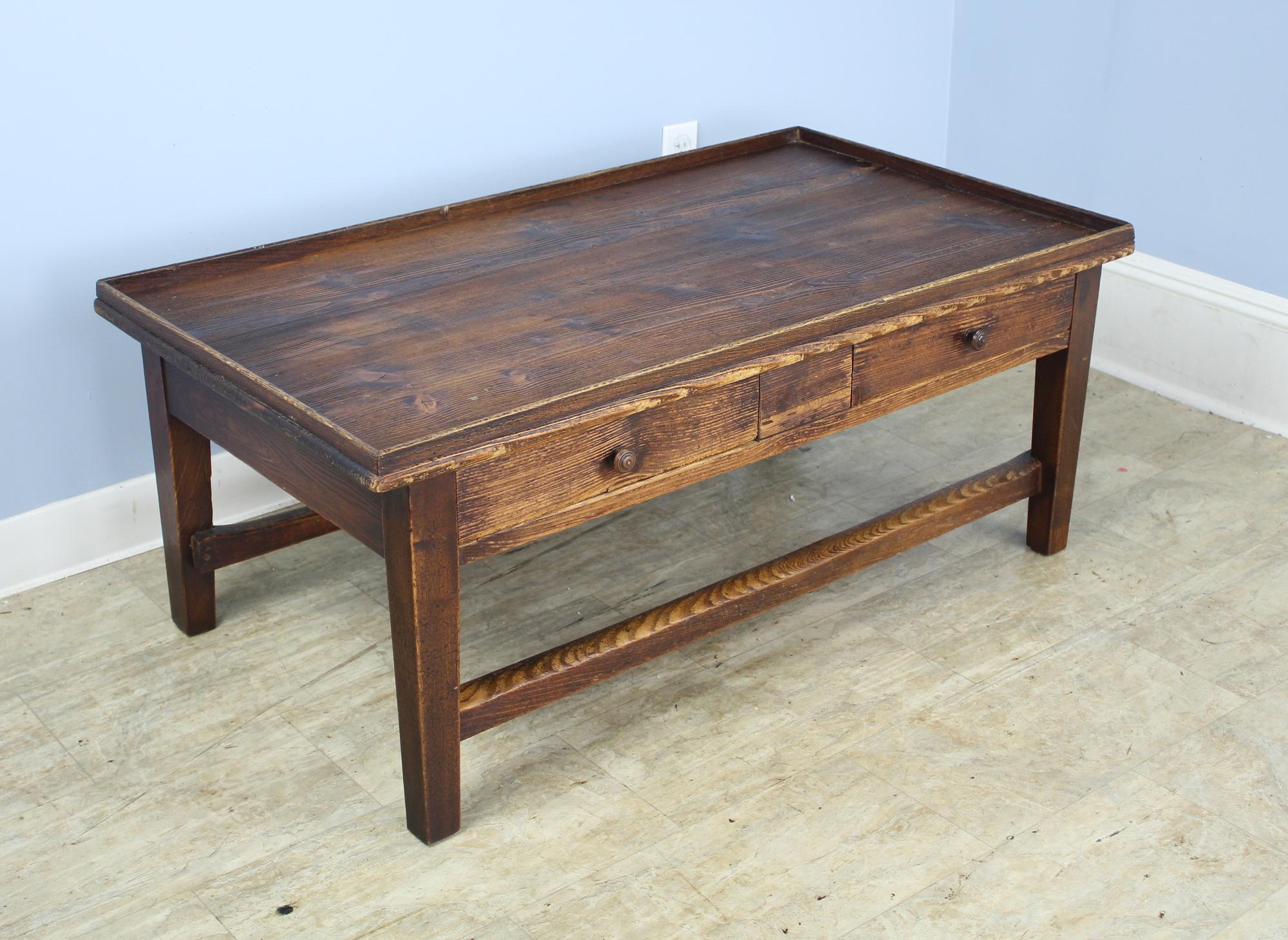 A solid pine tray-top coffee table with two drawers and rustic pine grain and color. The two supports between the legs have good wear and patina. The dramatic color contrast gives this piece a good country look.