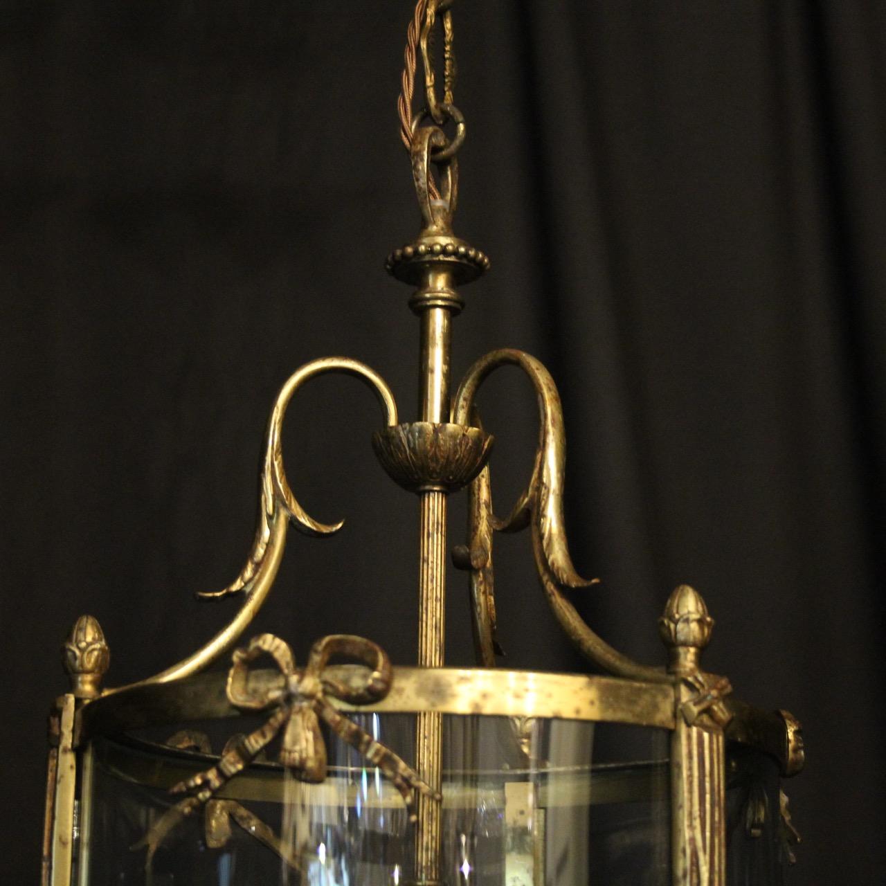 A French gilded cast bronze triple light antique hall lantern, the three scrolling light fittings surrounded by three sectional convex glass panels and held within an ornate scrolling framework with leaf side sections, pierced ribbon embellishments,