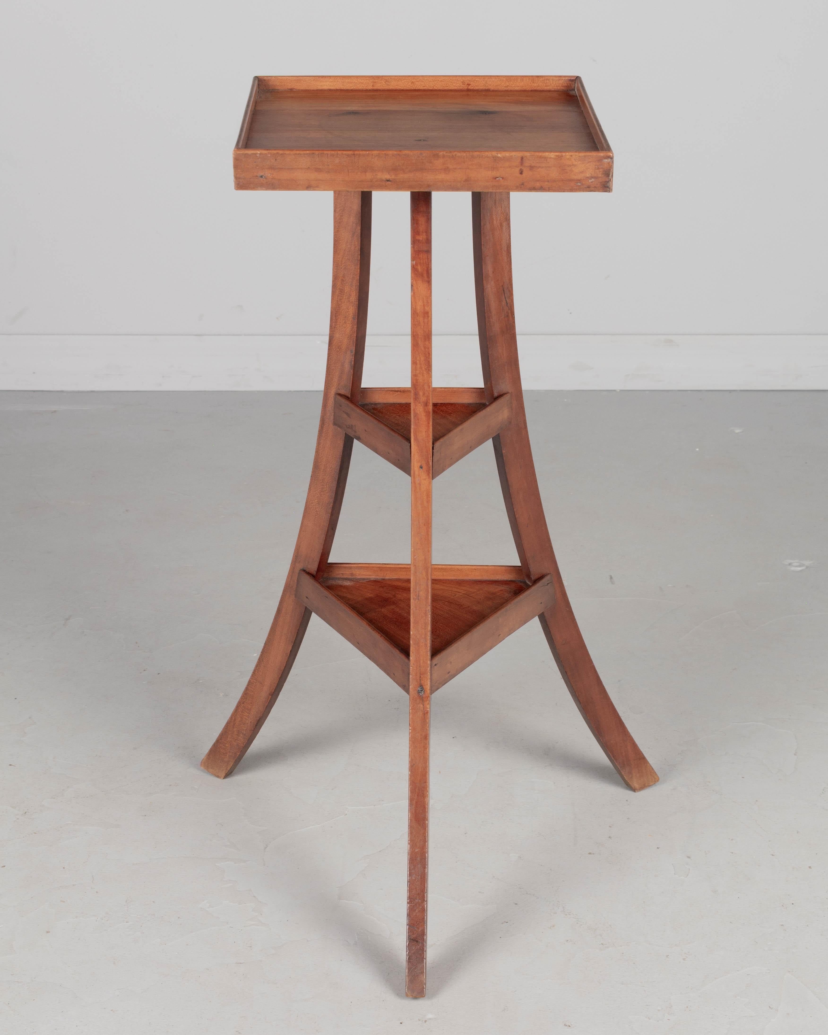 A French Arts & Crafts style small tripod accent table or pedestal, hand-crafted of solid cherry wood. Interesting form with square top and curved legs joined by triangle shelves. Circa 1940s
Dimensions: 17.5