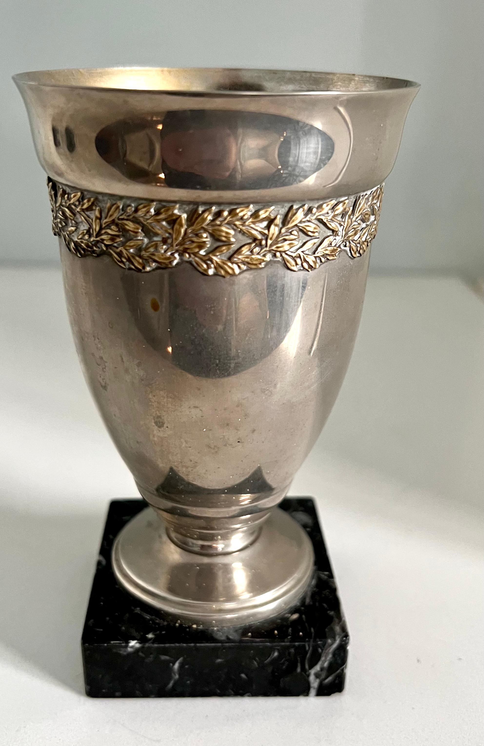 A wonderful Silver cup with a brass band detail on a marble or granite base. The cup, while perfectly suited for a small gathering of flowers or to store pencils on a desk, is actually a small trophy. While it isn't prominent, a small brass icon of