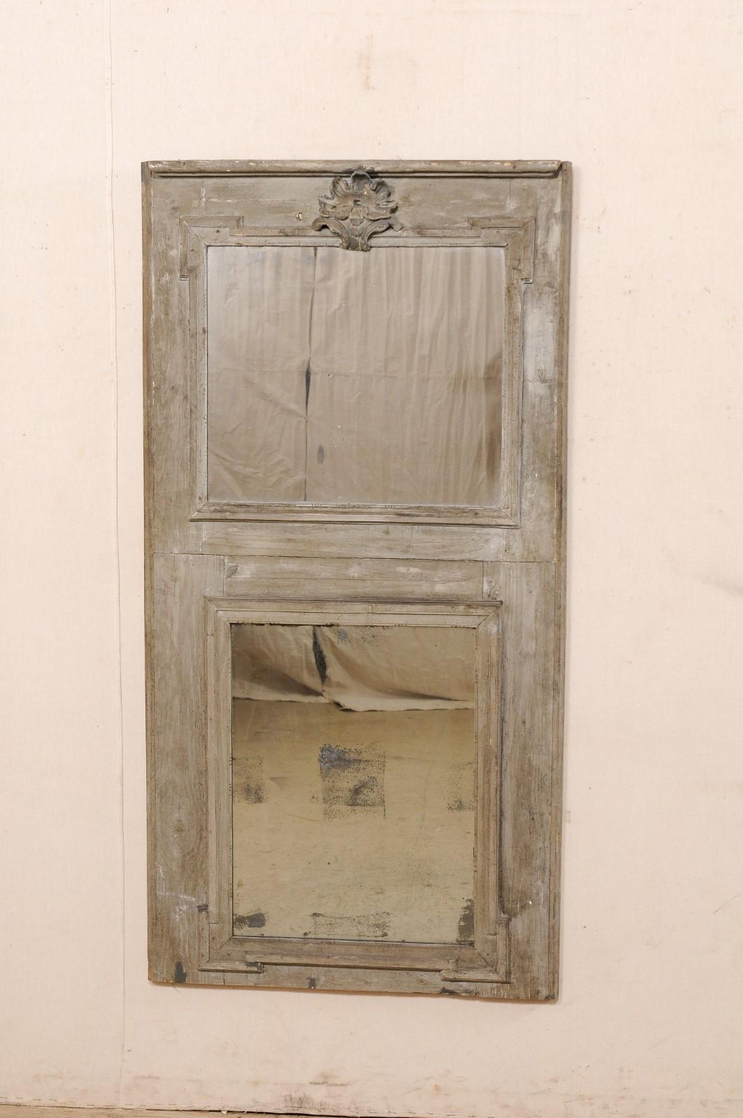 A French wooden trumeau mirror from the 19th century. This antique mirror from France features a vertically set rectangular-shape, with straight-line trim molding, with a mirror set within a top panel, over a secondary mirror below, with thick areas