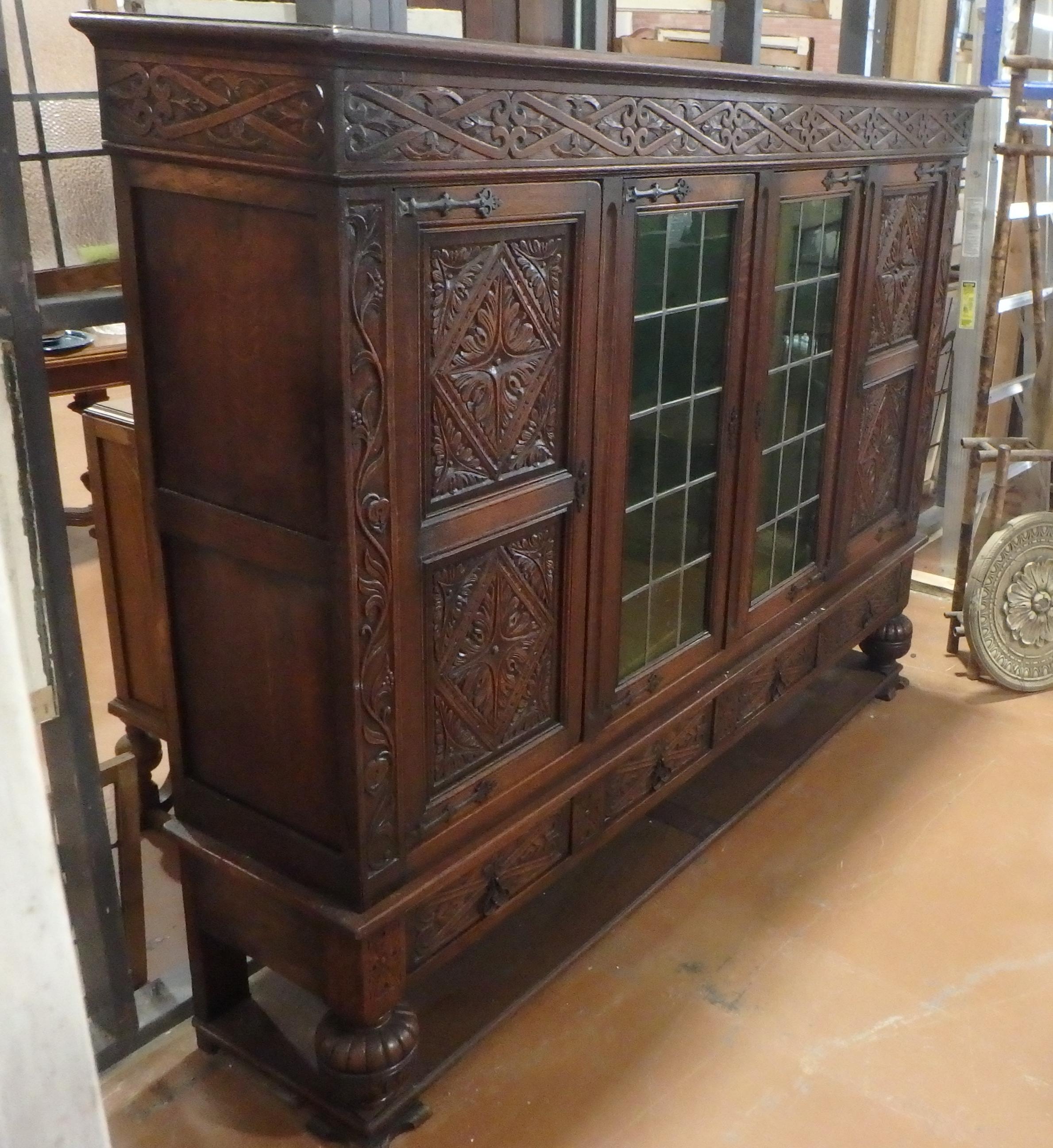 French Tudor style bookcase cabinet circa 1900 with deep hand carving and green leaded glass doors.