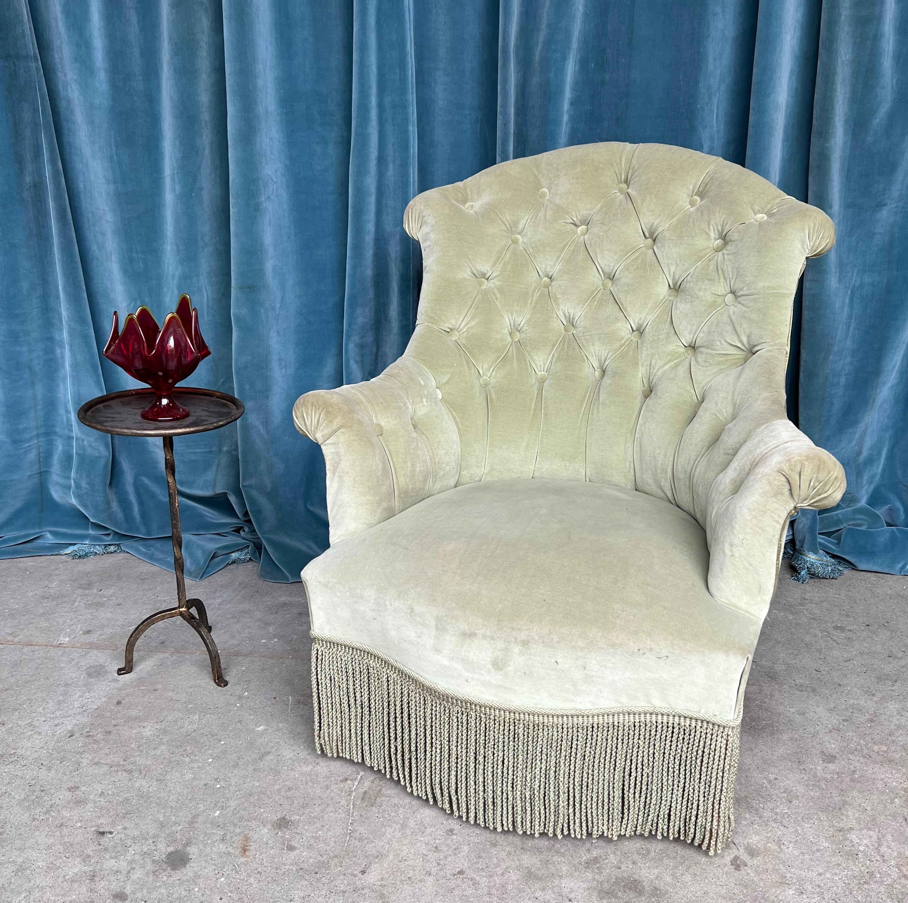 This late 19th century armchair, originating from the Napoleon III period, presents a blend of comfort and elegance. Upholstered in vintage sage green velvet, it features a tufted back that adds to its charm and sophistication. The matching bullion