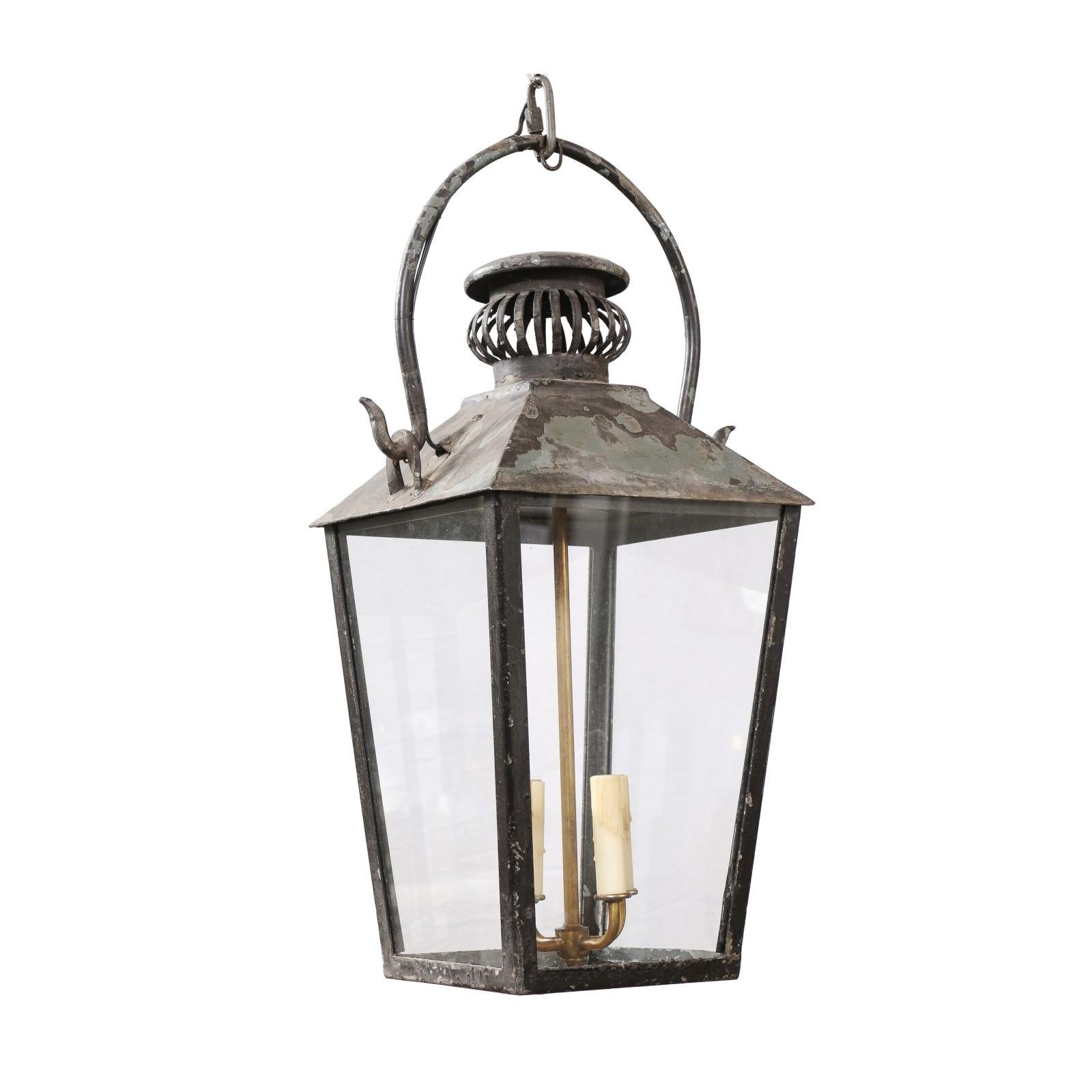 A French Turn of the Century iron lantern from circa 1900 with four lights, glass panels and pierced canopy. This French Turn of the Century iron lantern, dating back to circa 1900, is a testament to the timeless elegance and craftsmanship of early