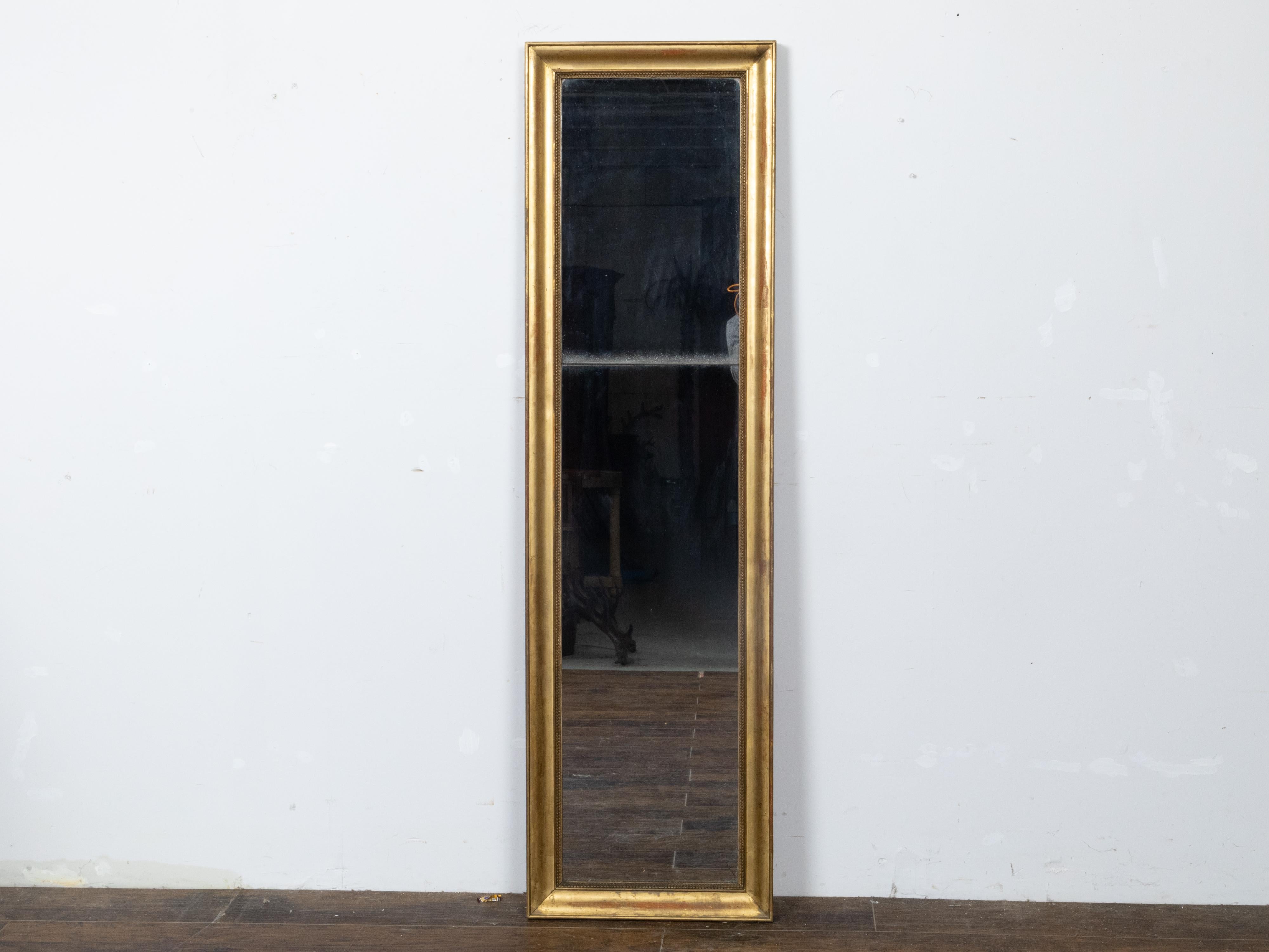A French Turn of the Century tall and narrow giltwood mirror from circa 1900 with split glass panels and carved frame. Step into the opulent world of early 20th-century French design with this exquisite Turn of the Century tall and narrow giltwood