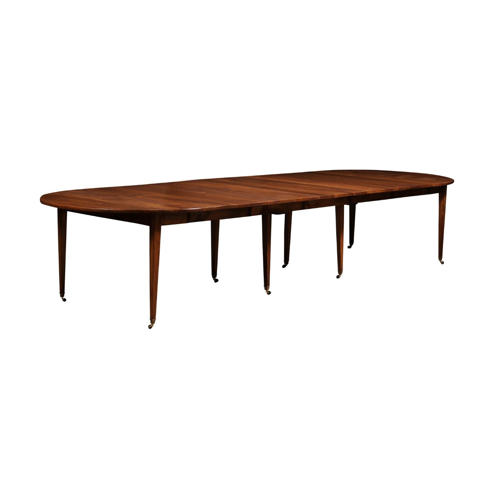 A French walnut oval extension dining room table from the early 20th century, with five leaves, tapered legs and casters. This exquisite French walnut oval extension dining room table from the early years of the 20th century marries classic elegance
