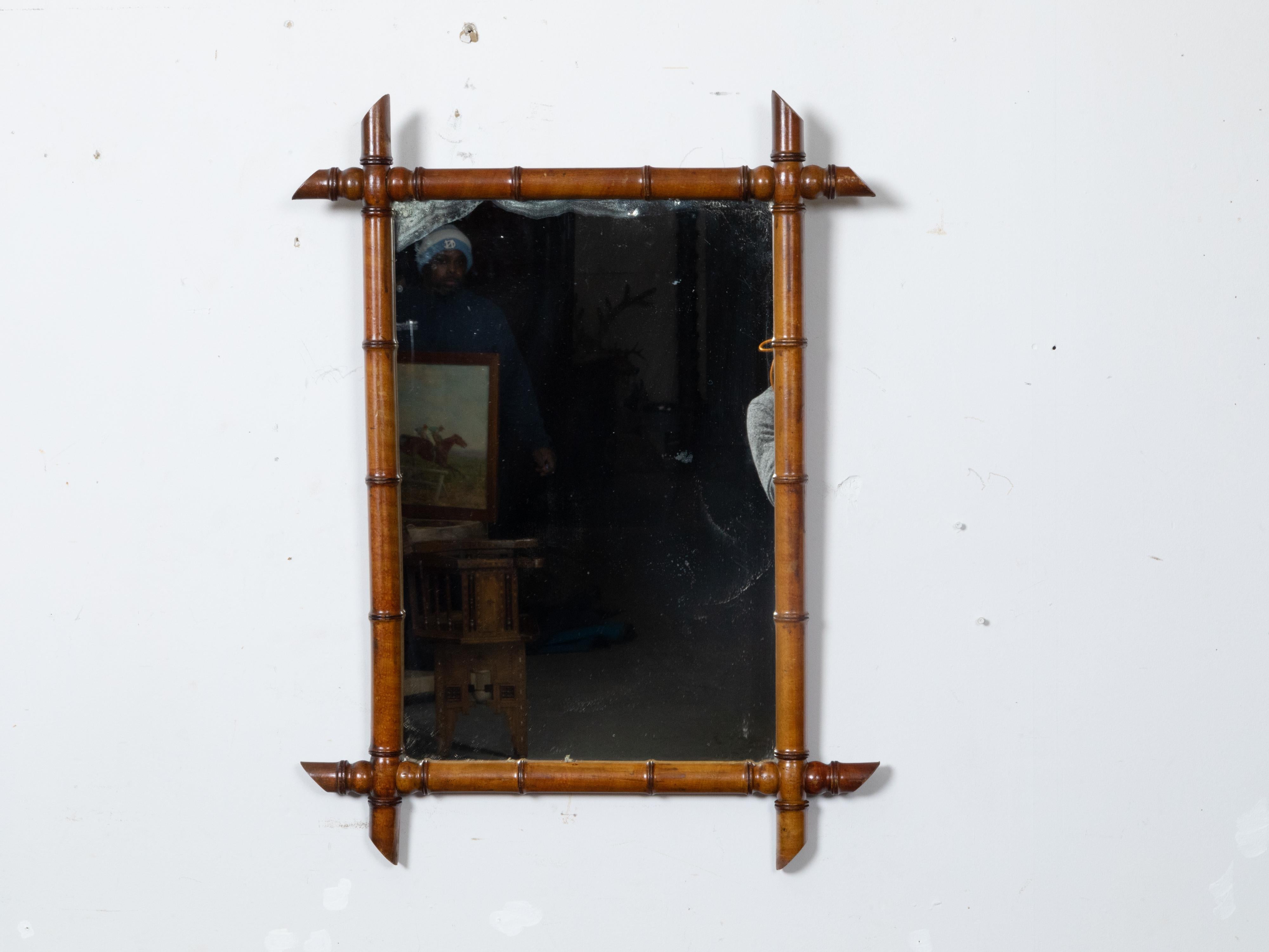 A French Turn of the Century brown faux bamboo wall mirror, dating back to circa 1900, presenting intersecting corners, rich brown color, and traces of aging on the mirror plate.

The mirror's wooden frame, skillfully crafted to resemble bamboo,