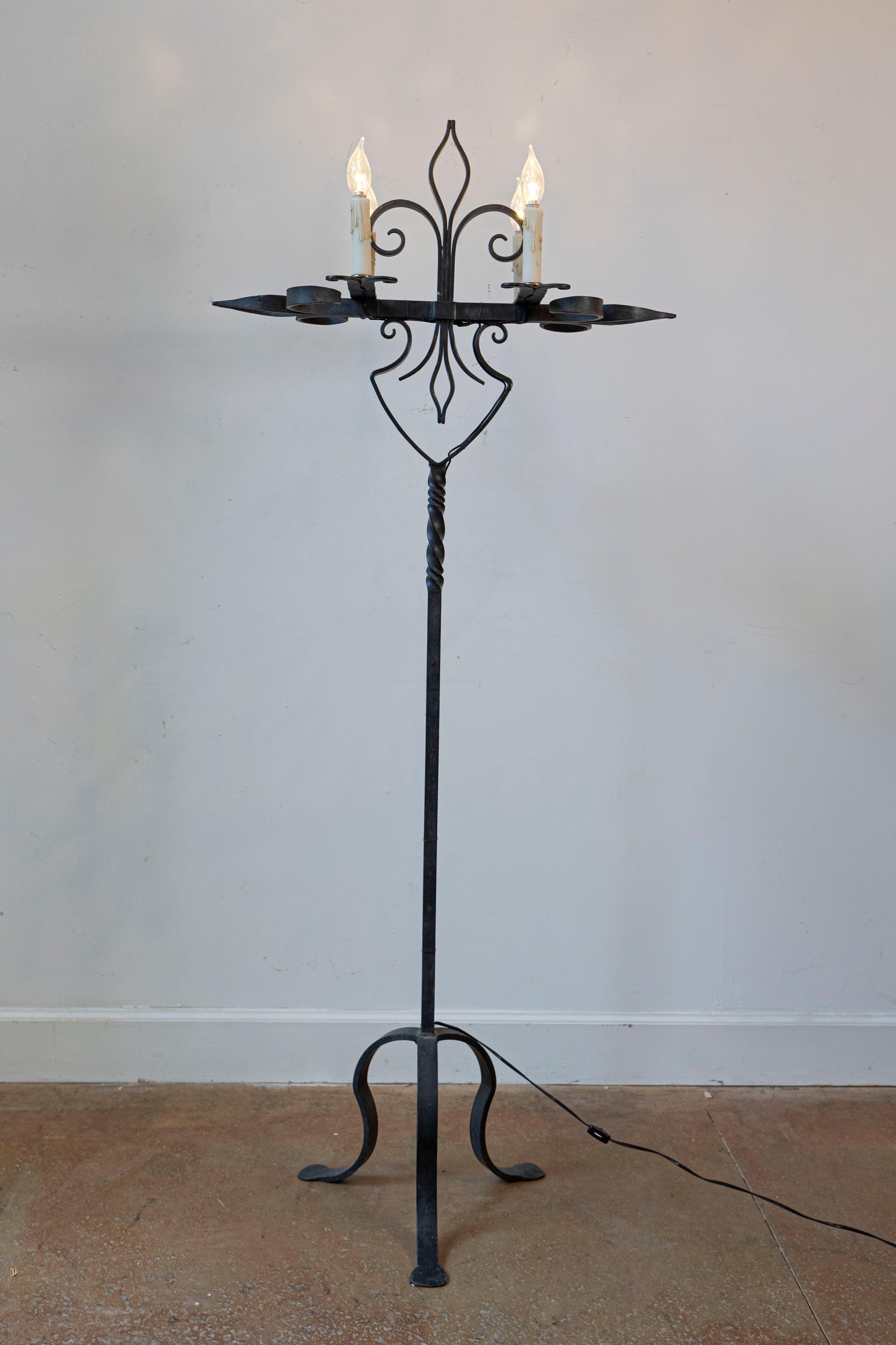 Lámpara de pie de cuatro luces de hierro forjado estilo candelabro francés de principios del siglo XX, con motivos de flores de lis, detalles retorcidos y base de trípode. Creada en Francia durante los primeros años del siglo XX, esta lámpara de