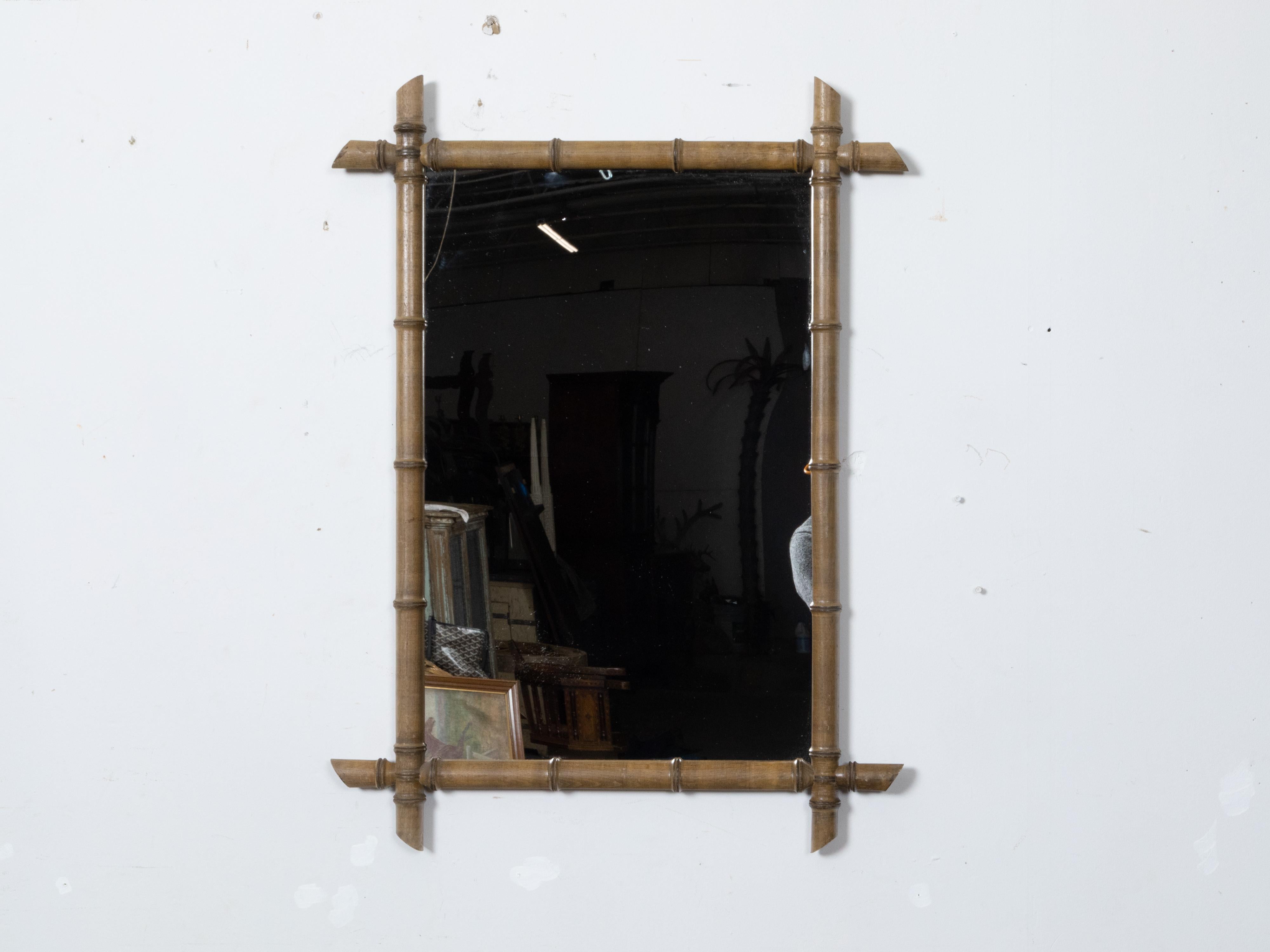 This French Turn of the Century wooden faux bamboo wall mirror, dating back to circa 1900, features intersecting corners, a light brown finish, black accents, and an attractive patina. The mirror combines elegance and simplicity in a harmonious
