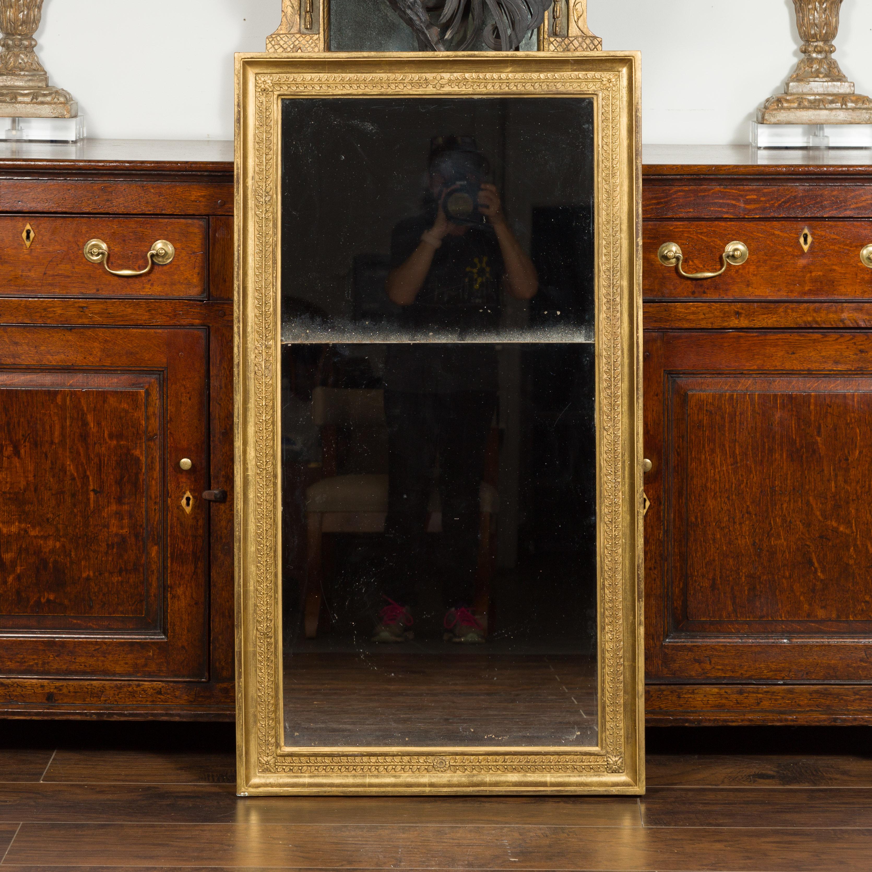 A French giltwood rectangular mirror from the early 20th century, with foliage and rosette motifs and split mirror. Created in France at the turn of the century, this gilt mirror features an elegant linear frame accented with a calm frieze of