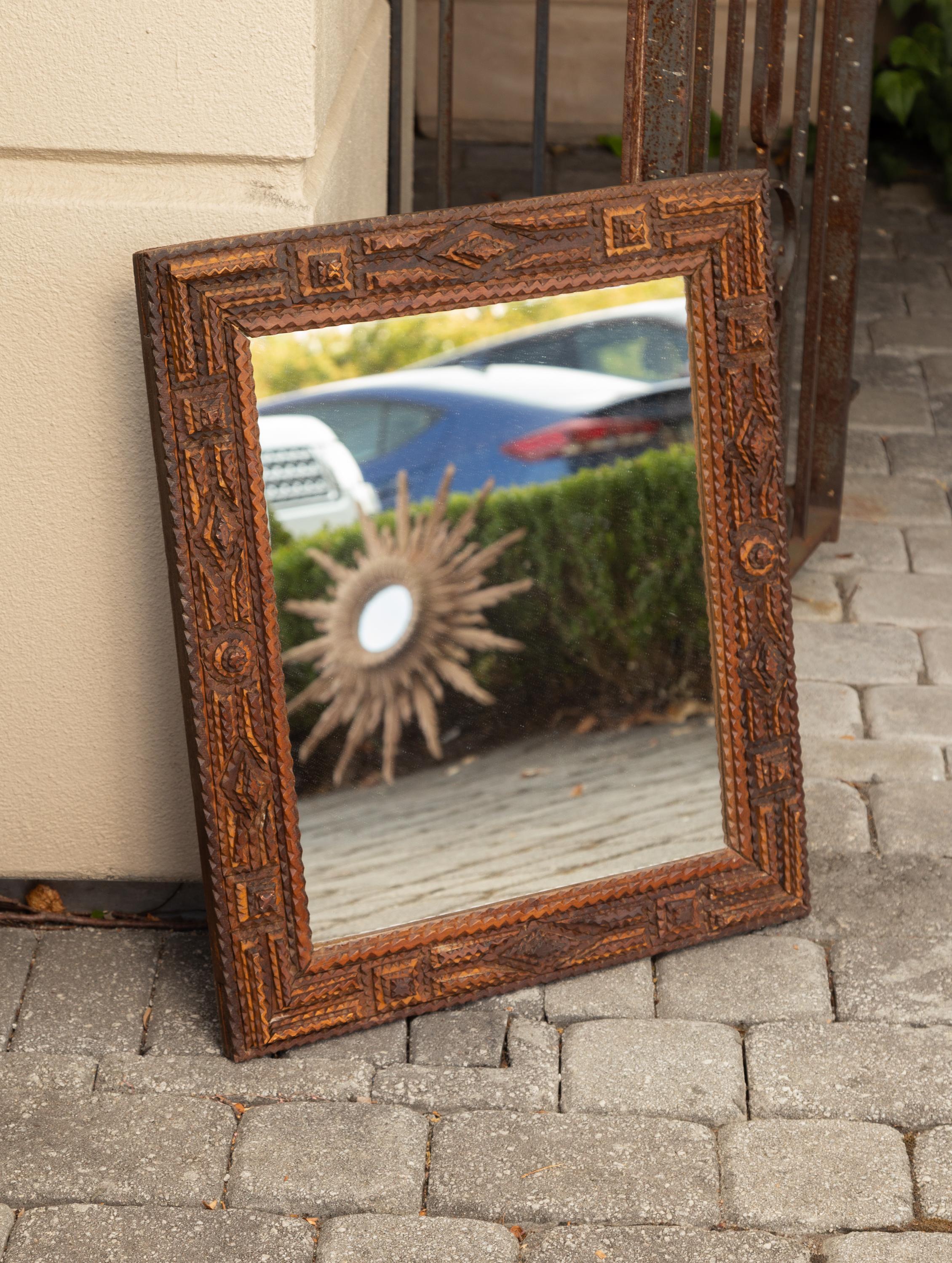 A French hand carved Tramp Art folk wall mirror from the early 20th century, with raised motifs. We have a second one available. Born in France during the transition of the turn of the century, this charming wooden mirror presents the stylistic