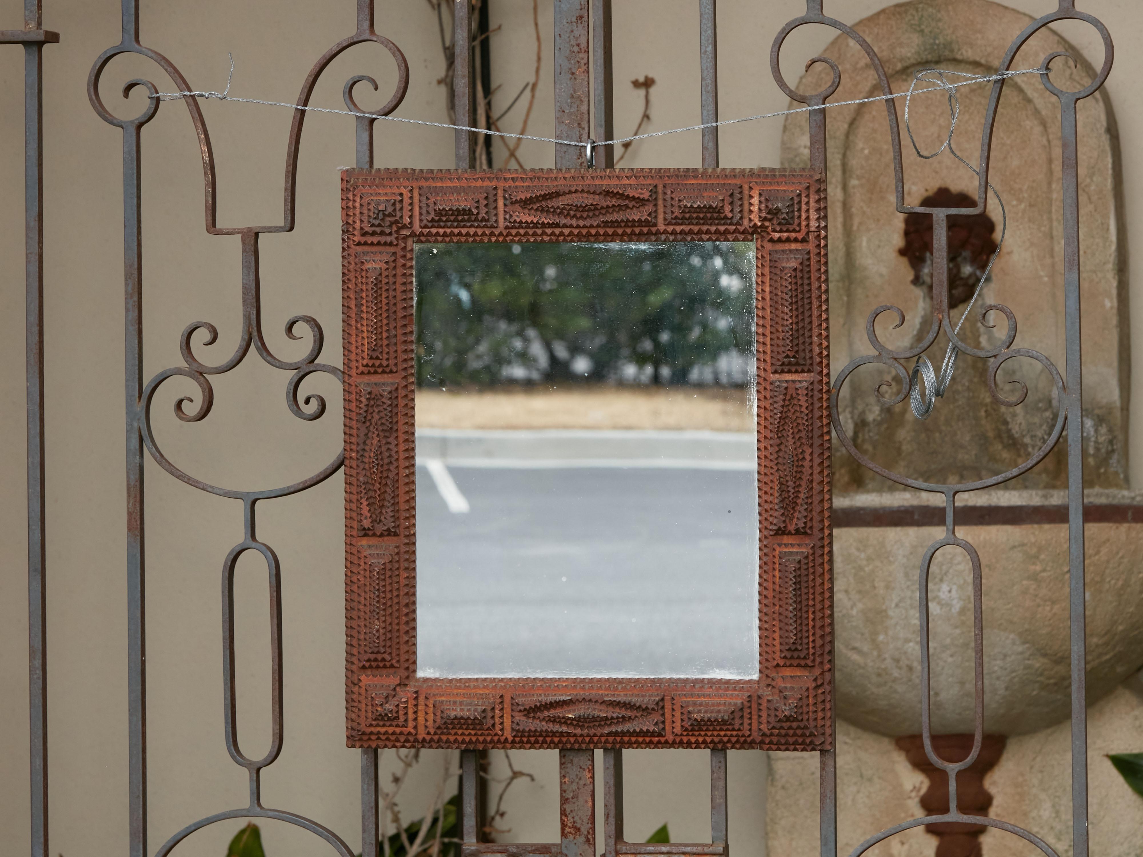 A French hand carved Tramp Art folk wall mirror from the early 20th century, with raised motifs. Created in France during the Turn of the Century period which saw the transition between the 19th to the 20th, this charming wooden mirror presents the